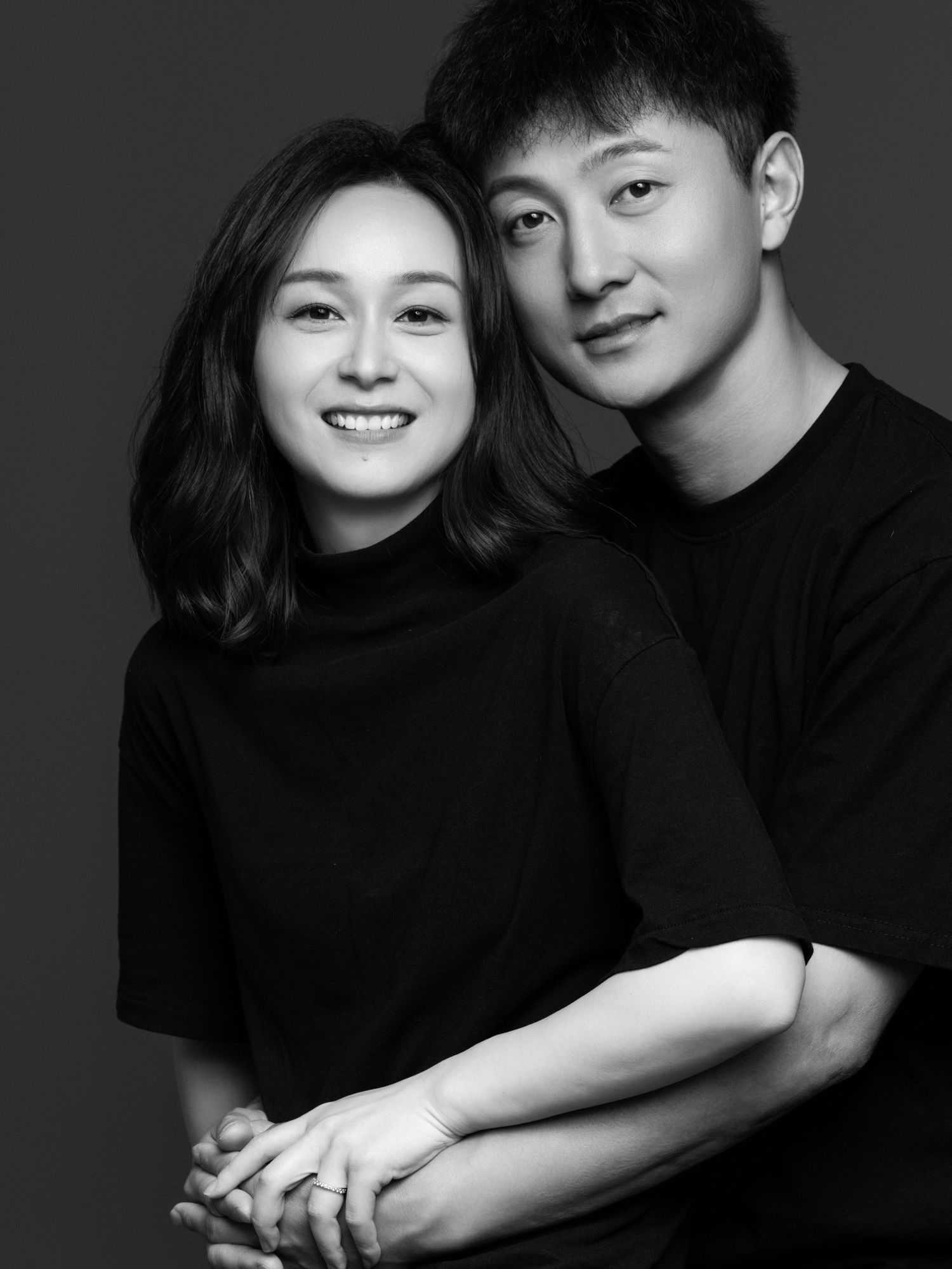Romantic black and white studio photo of a couple embracing while wearing black clothing.