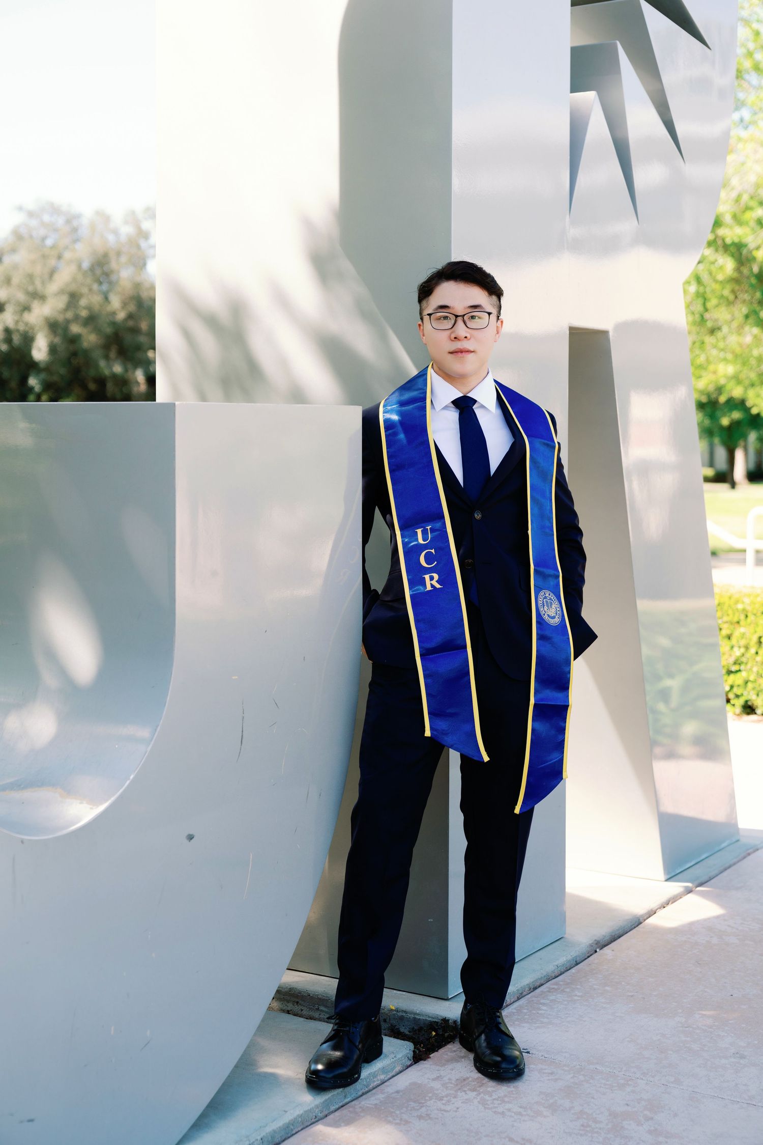 Graduate in blue stole stands against white architectural columns in natural lighting.