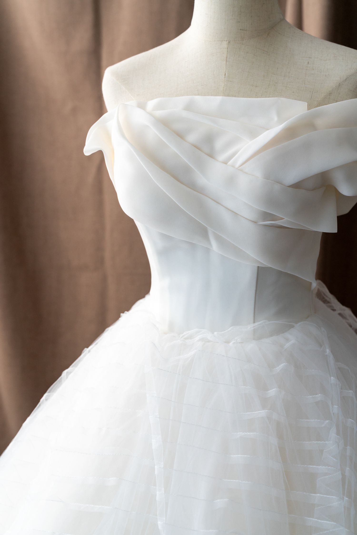 Off-shoulder white wedding gown with draped organza bodice detail.
