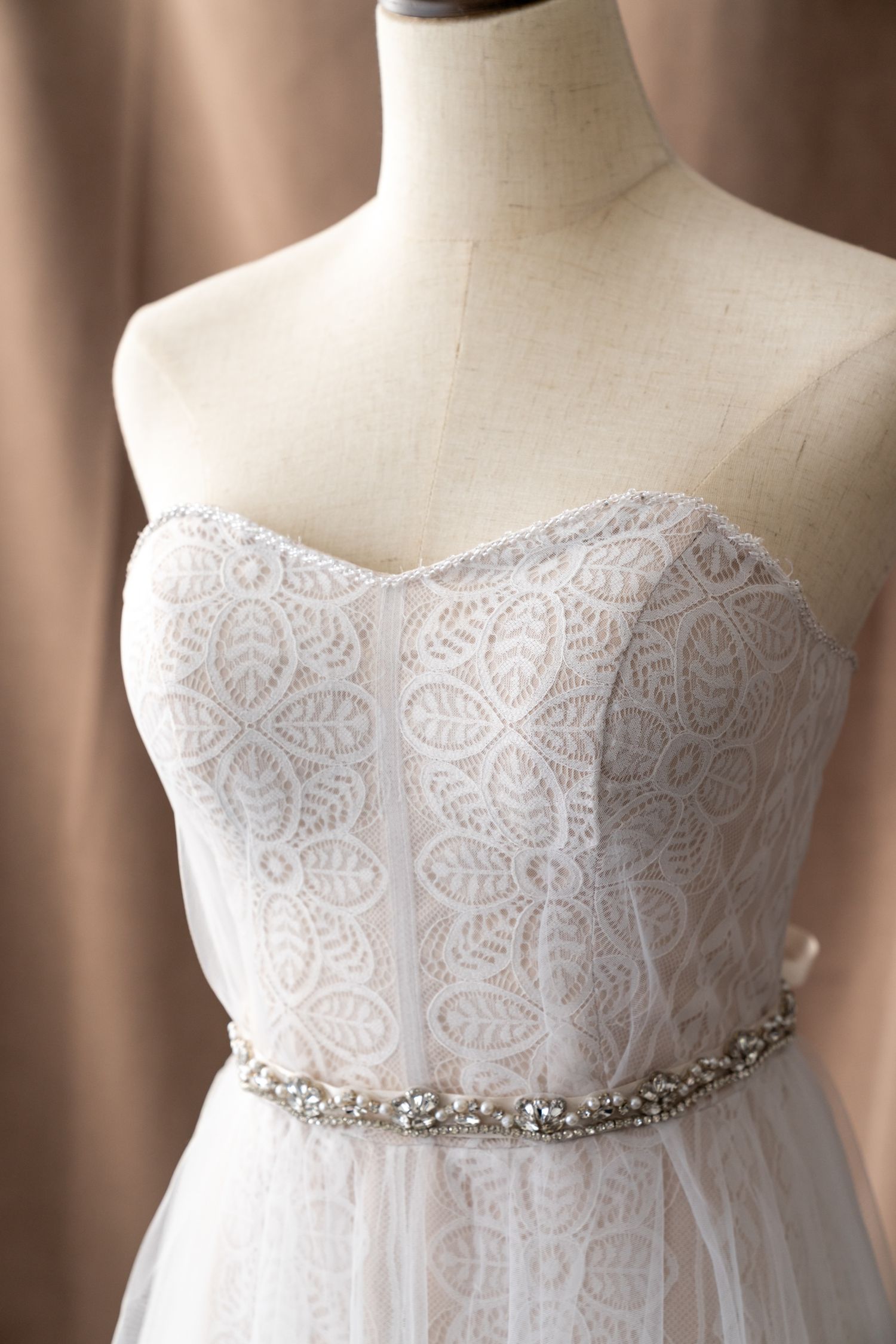 Close-up of wedding dress bodice featuring delicate lace pattern and crystal belt detail.