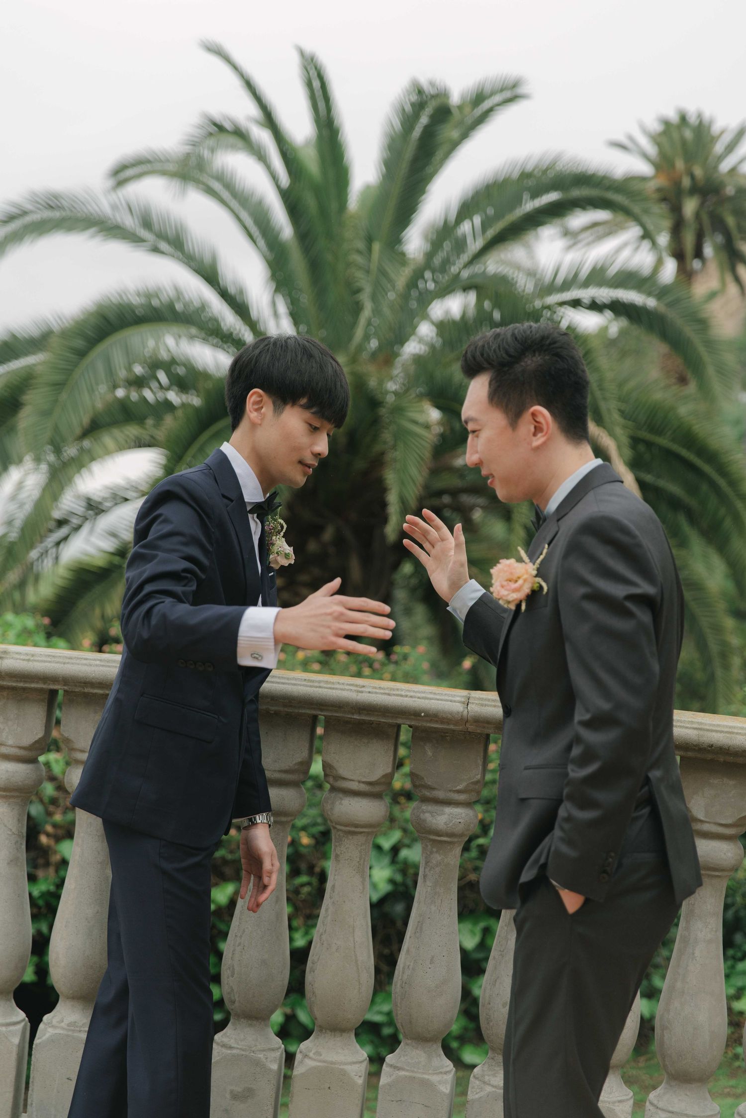 Two people in formal attire share an animated conversation by a stone balustrade.