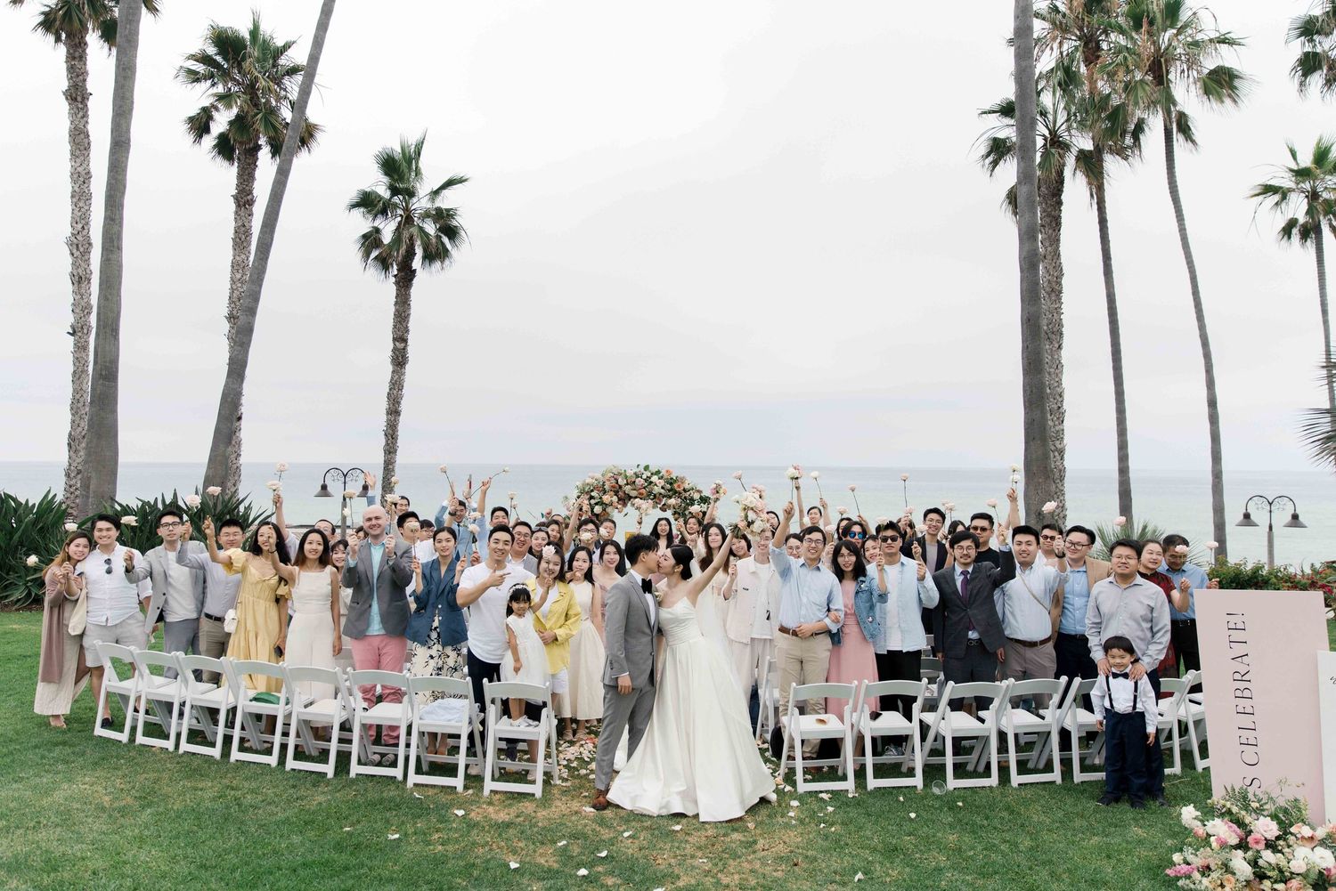 Outdoor wedding ceremony setup with white chairs and palm trees along a beachfront venue.