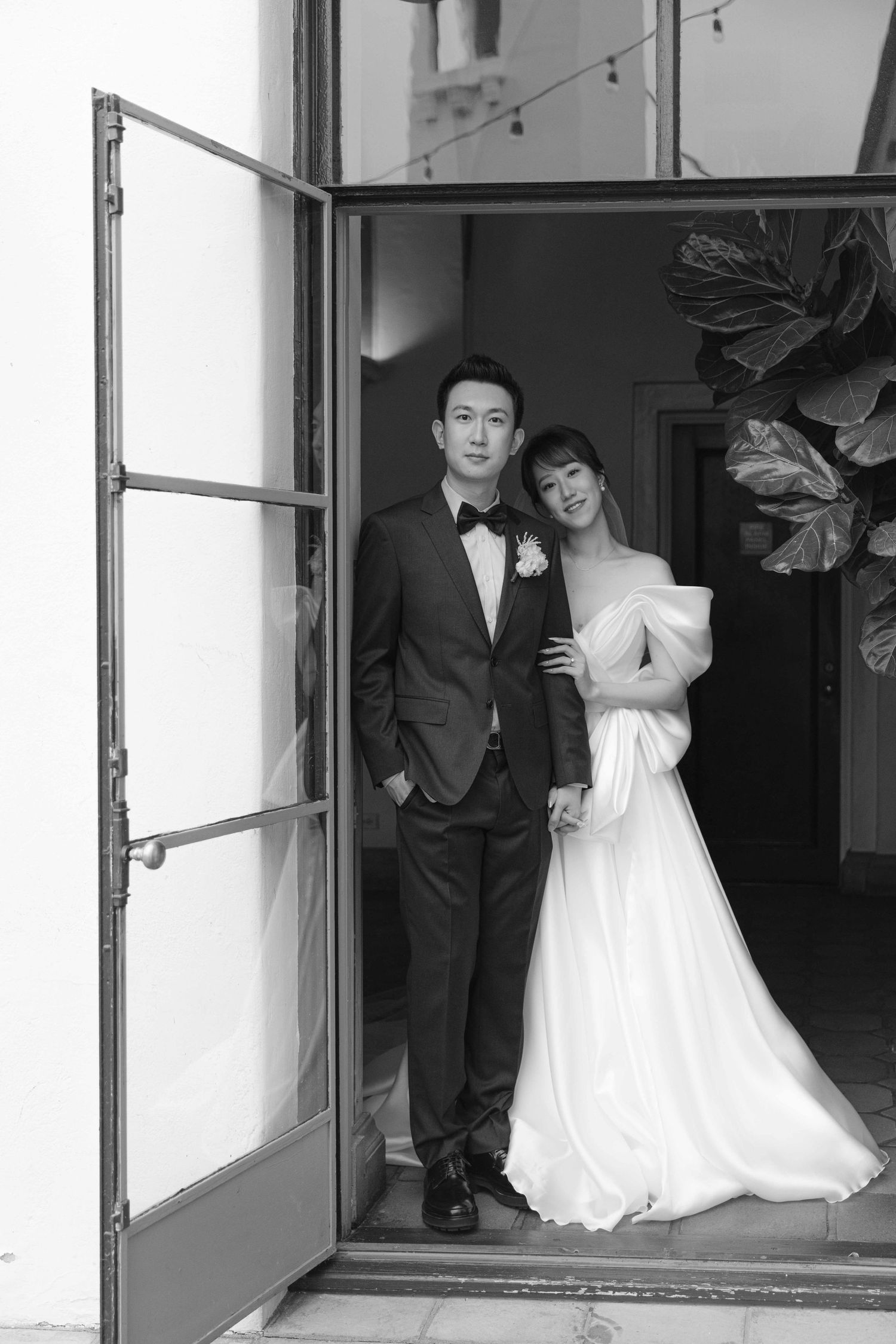 Wedding couple posing in doorway with dramatic black and white lighting.