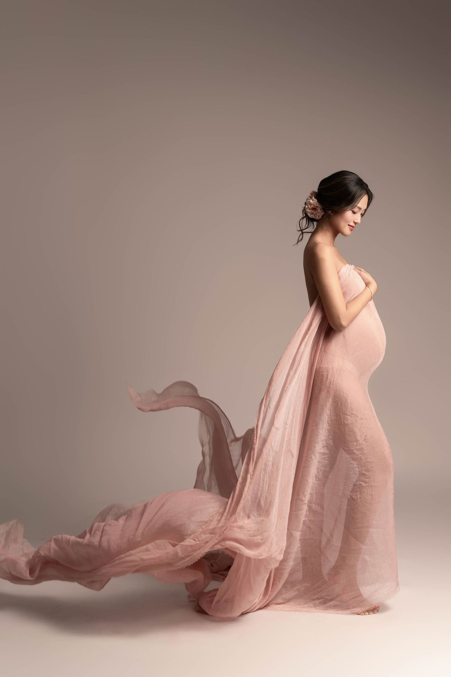 Graceful maternity silhouette wrapped in flowing pink chiffon fabric.