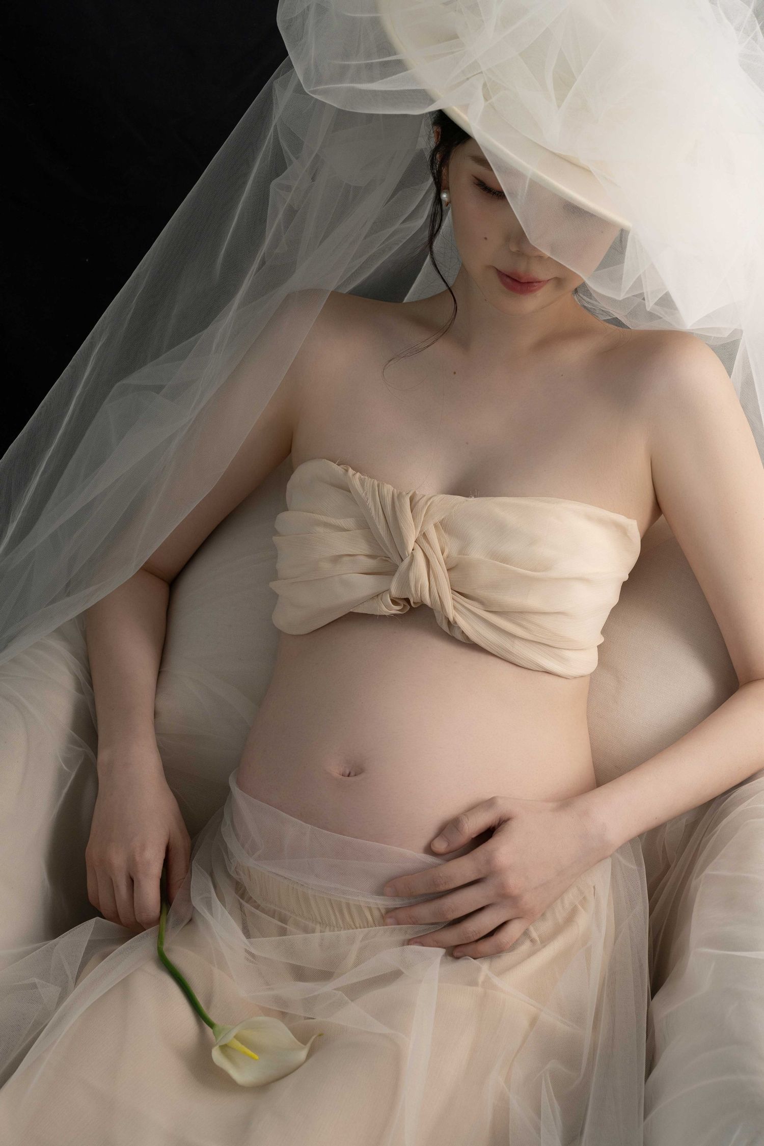 Ethereal maternity photoshoot featuring soft tulle fabric and delicate styling against light background.