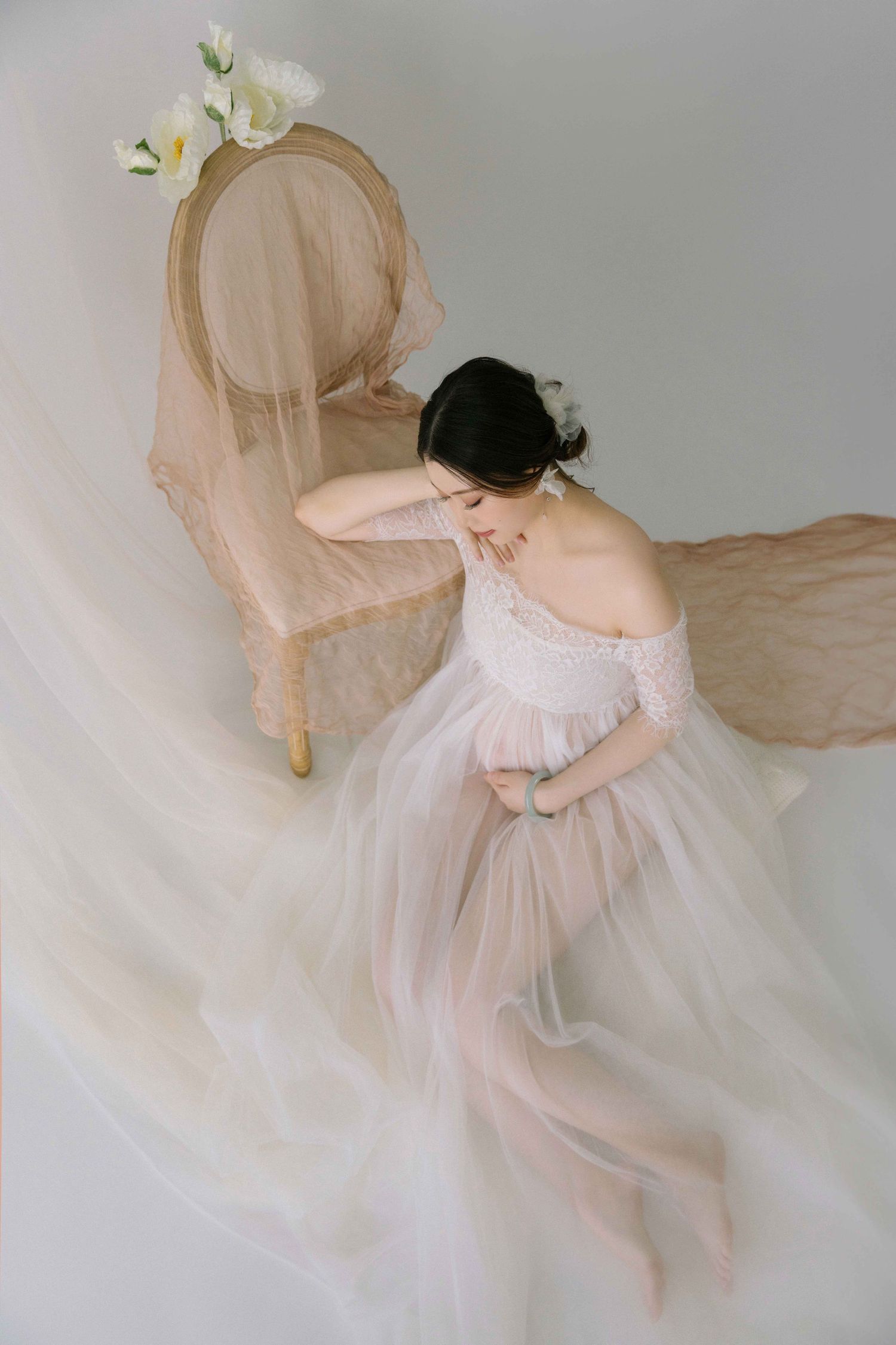 Dreamy maternity photos with flowing sheer fabric and white floral accents.