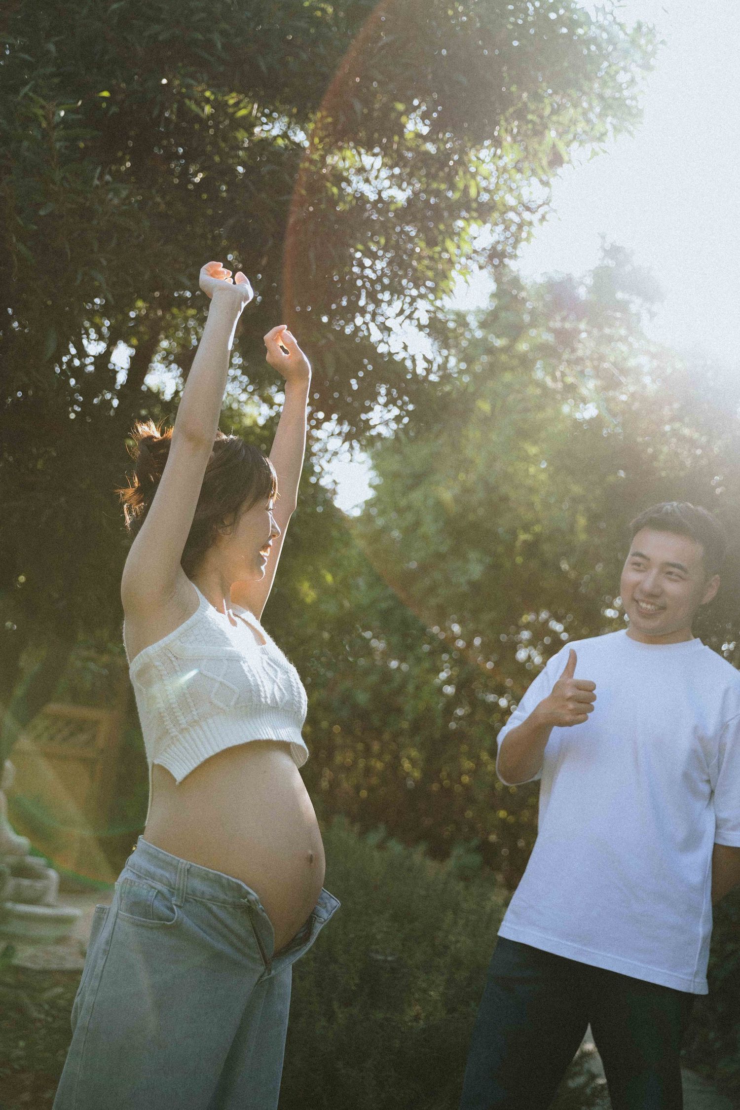 Joyful outdoor maternity photos with couple dancing in sunlit garden setting.