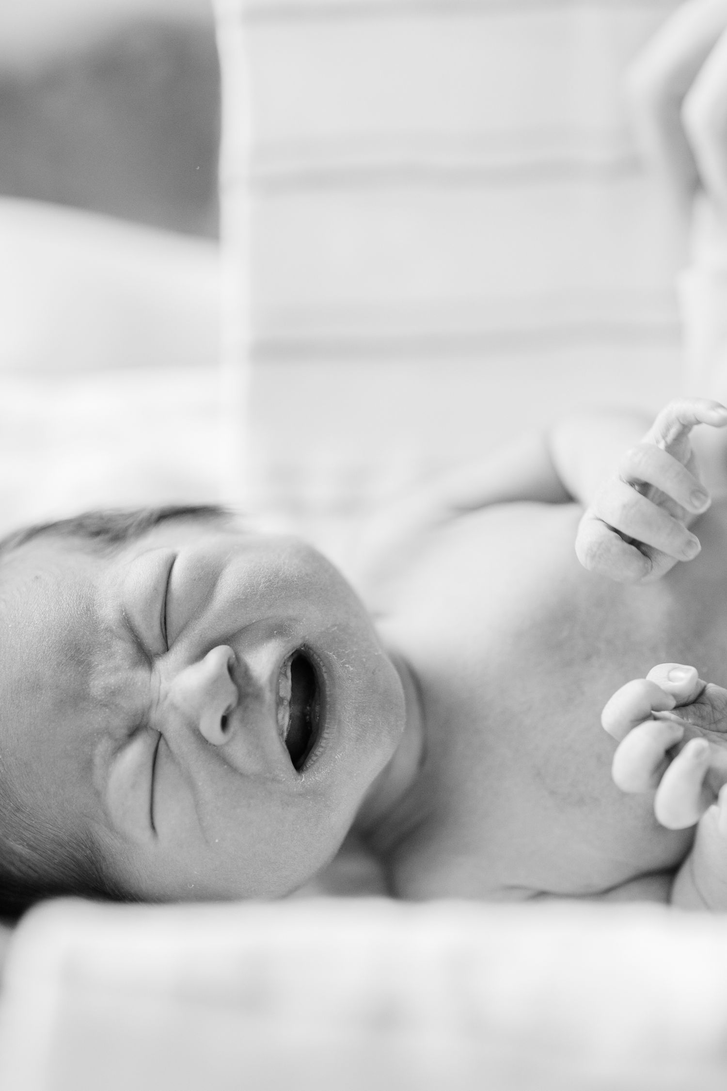 Close-up profile view of a newborn baby lying on white hospital bedding.
