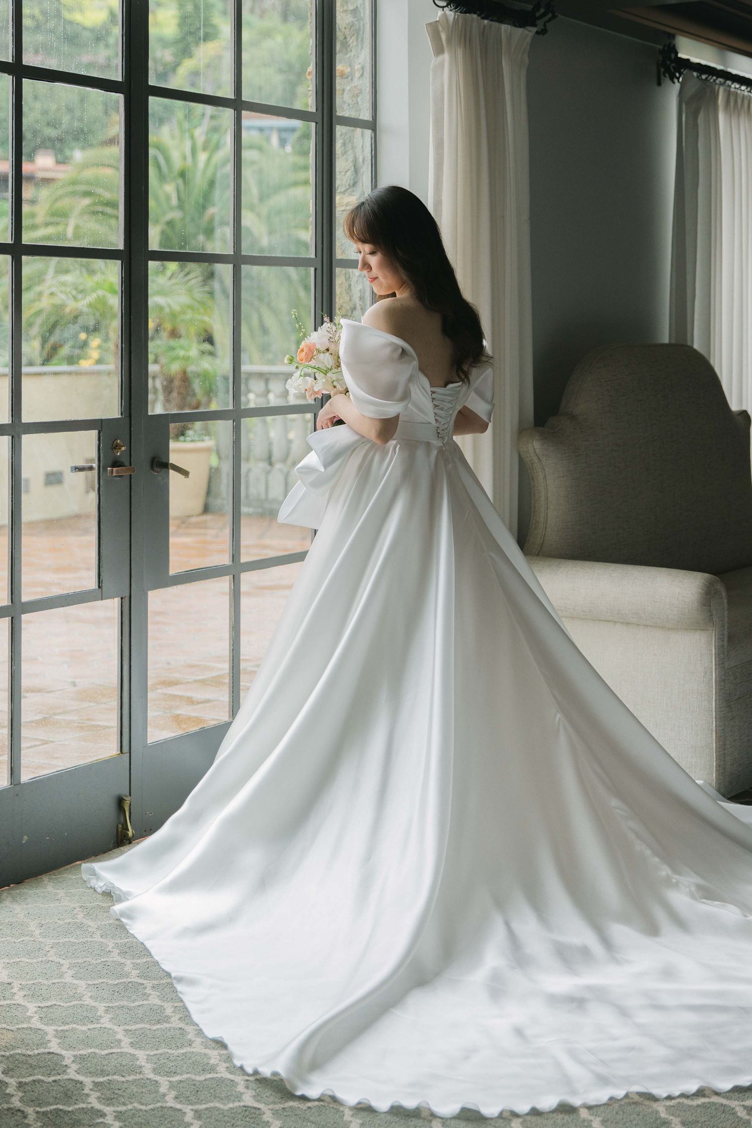 Dramatic full-length white wedding gown with flowing train photographed against floor-to-ceiling windows.