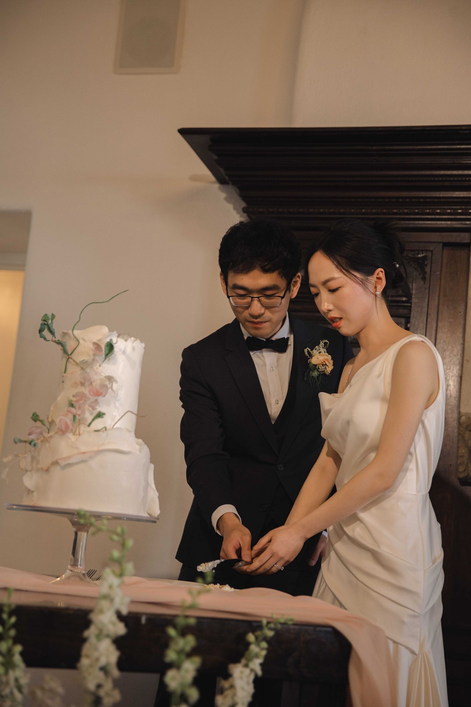 A couple in wedding attire cuts their elegant floral wedding cake together.