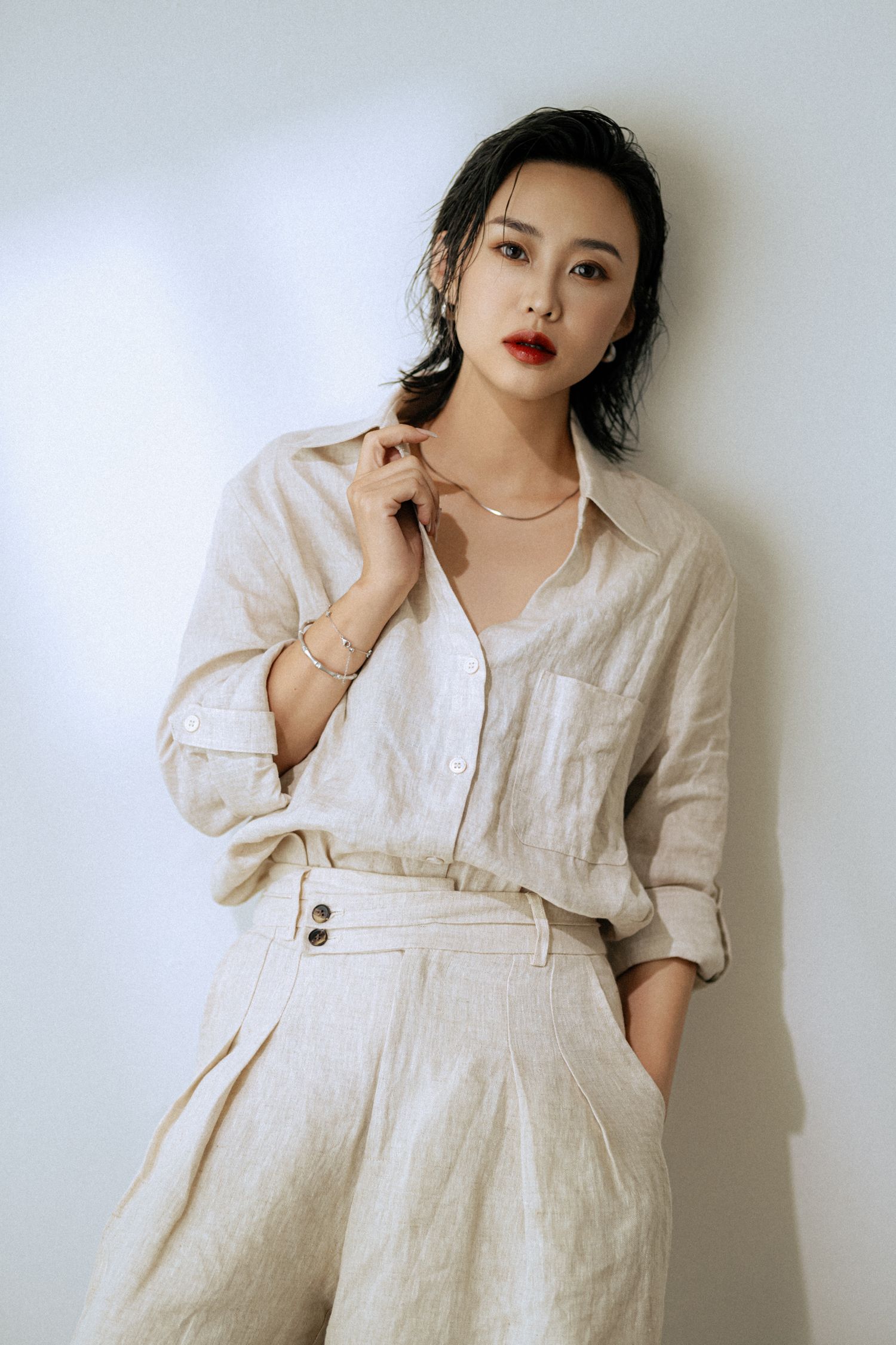 Fashion model poses in cream linen outfit against white wall showing elegant minimalist style.