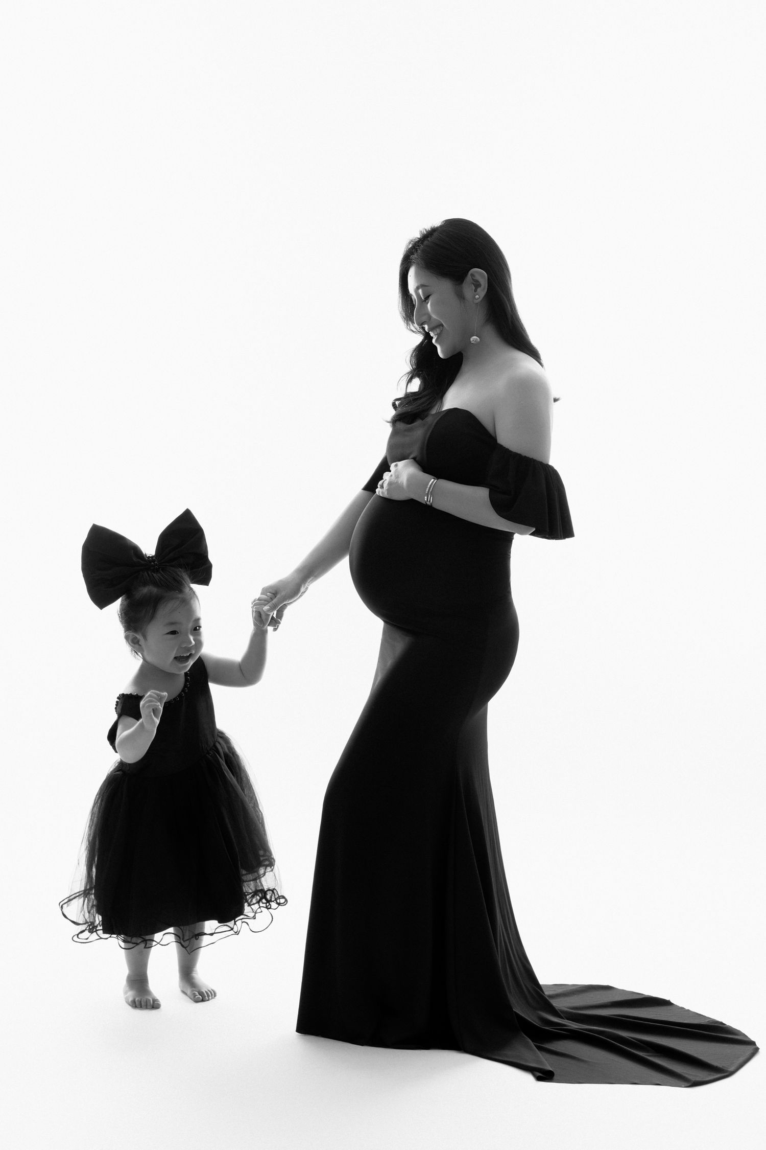 Silhouette of mother and child in matching black dresses holding hands.