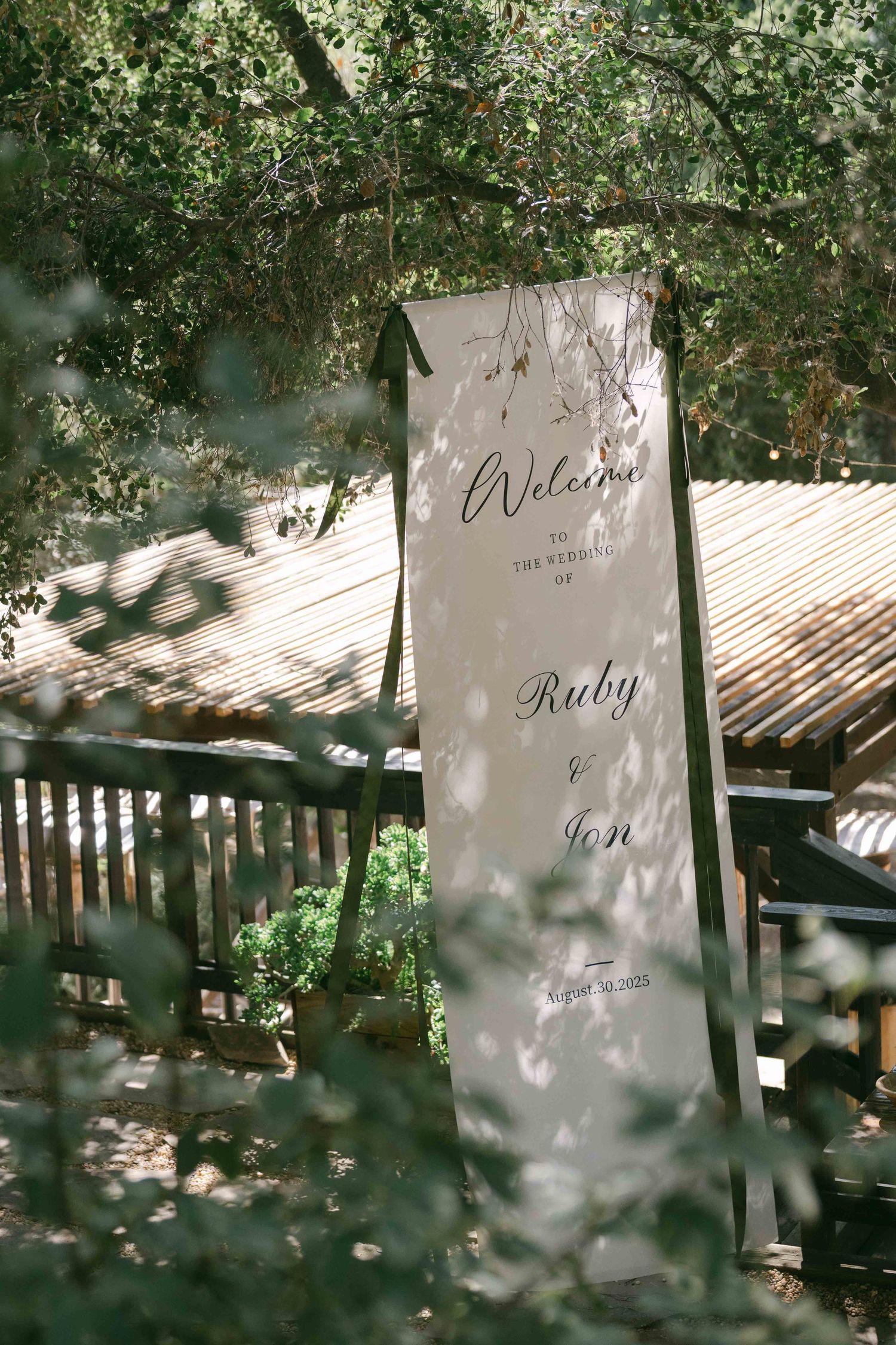 Elegant wedding welcome sign displayed in a garden setting with natural lighting.