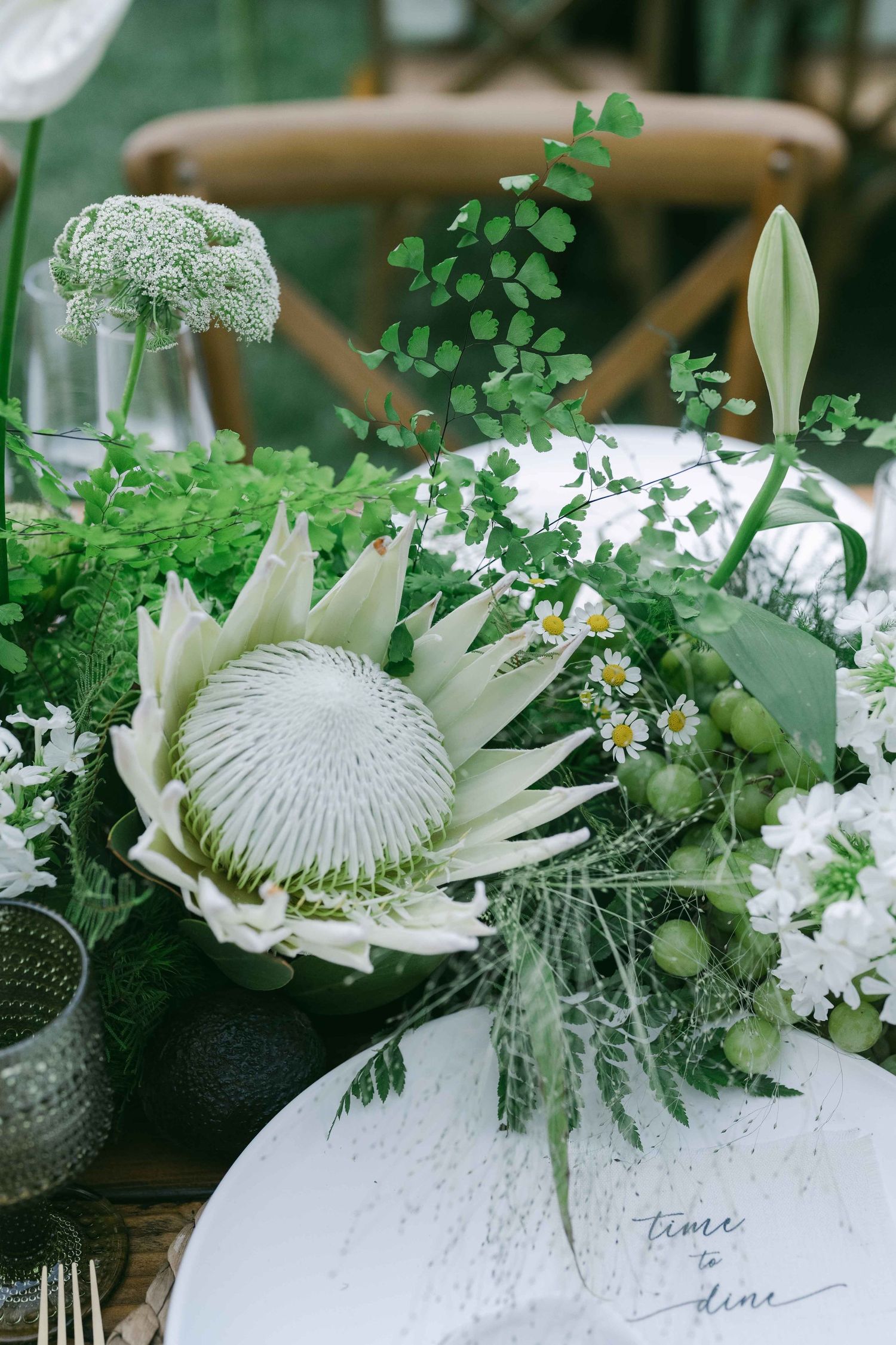Elegant white protea flowers and greenery arranged in modern vases for a wedding table setting.