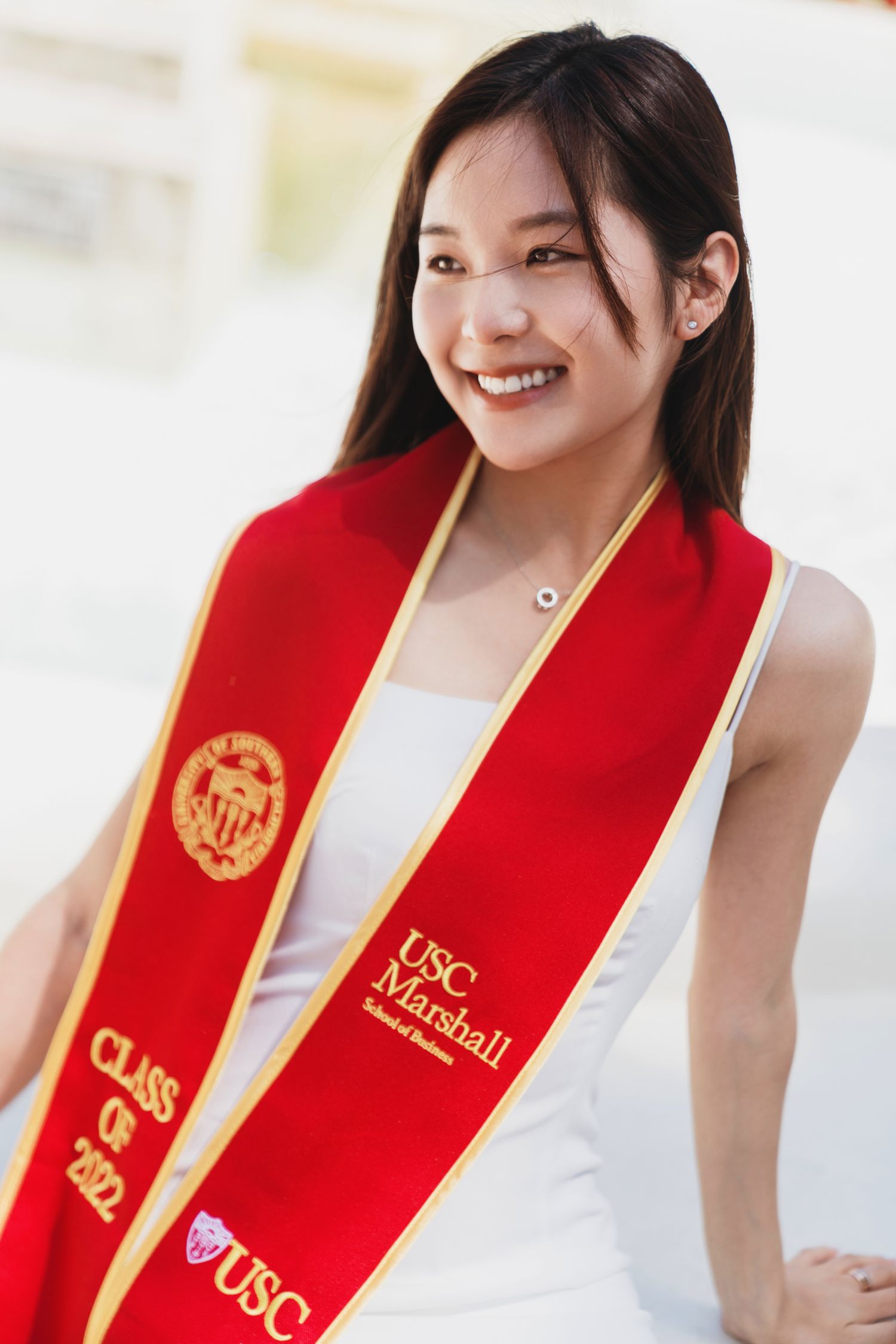 Graduate wearing USC red graduation stole and white dress smiling at camera.
