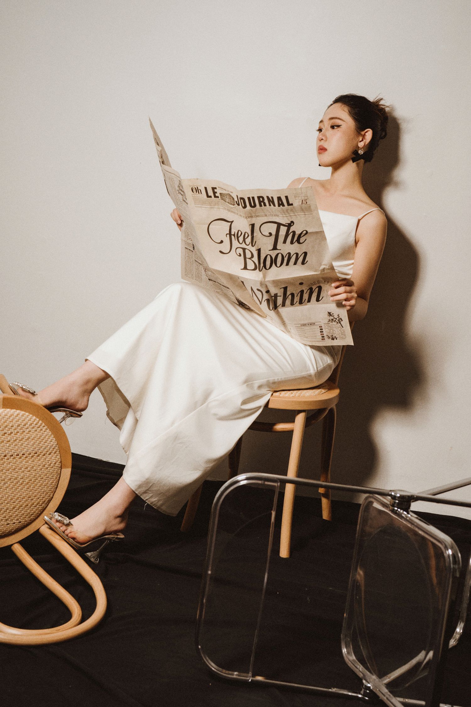 Vintage-inspired fashion scene with newspaper and wooden chair in studio setting.