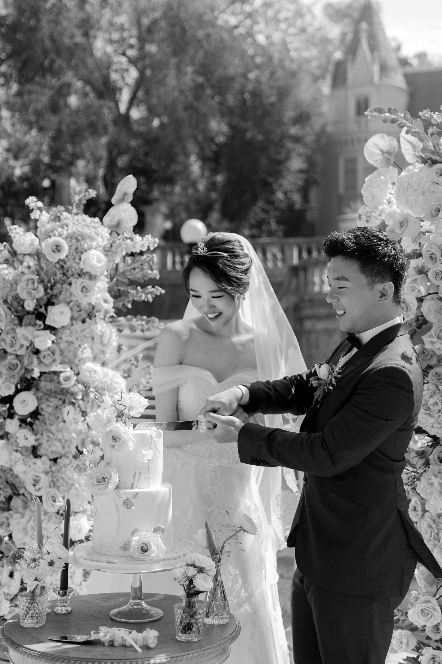 An elegant outdoor wedding reception setup with white floral arrangements and cake display.