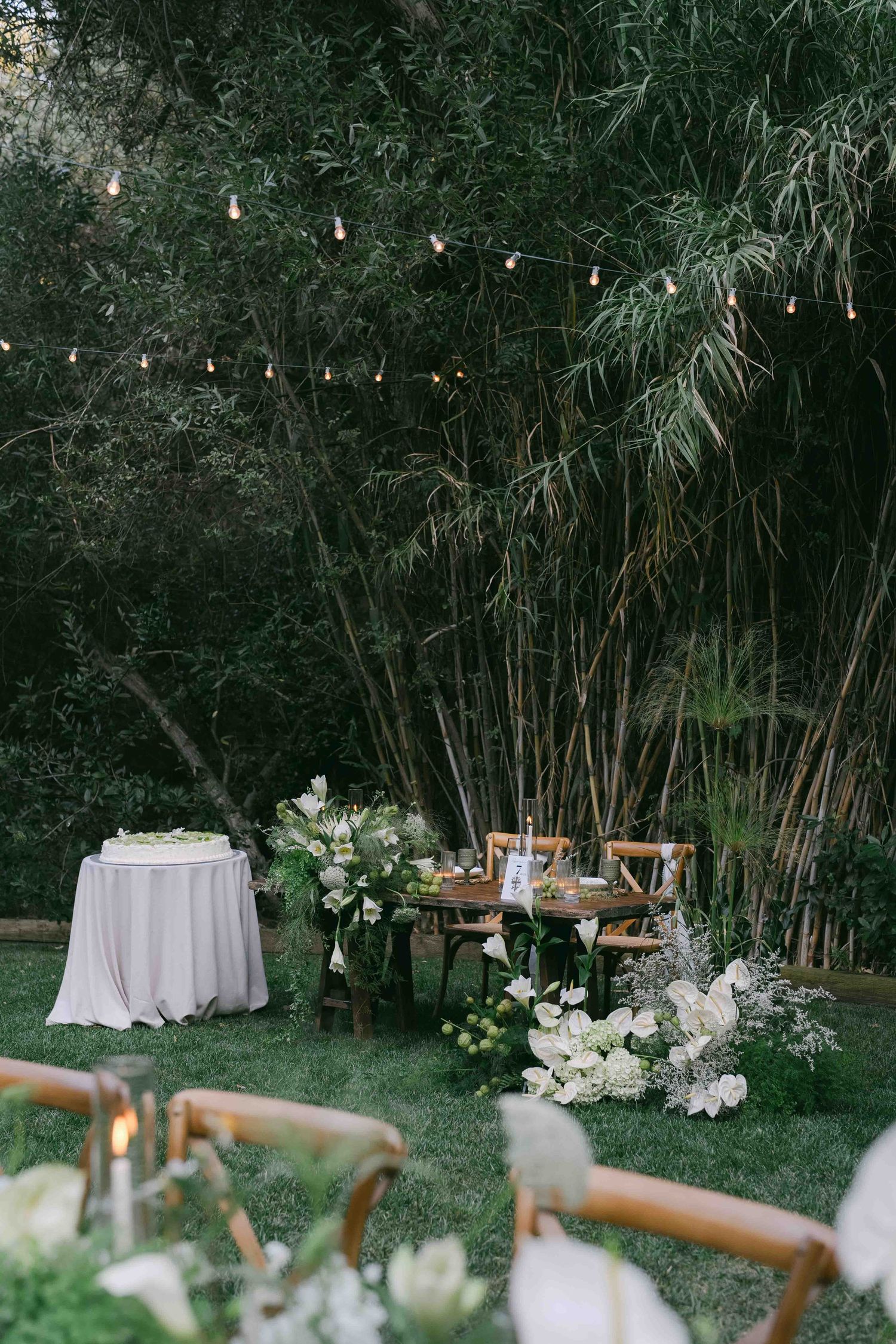 Elegant outdoor wedding reception setup with white tablecloths and bamboo grove backdrop.