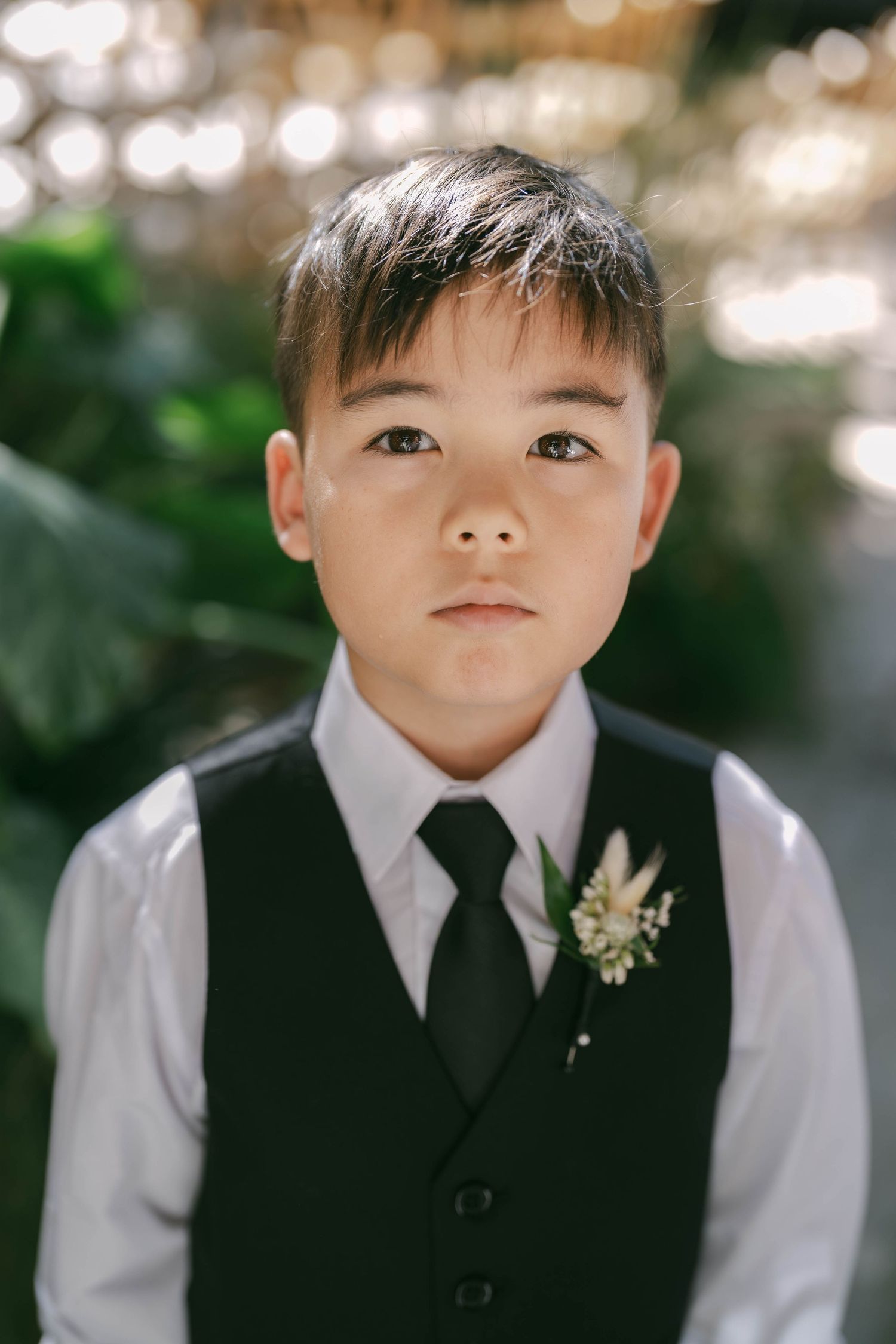 Young ring bearer in formal black vest and white shirt with boutonniere at wedding ceremony.