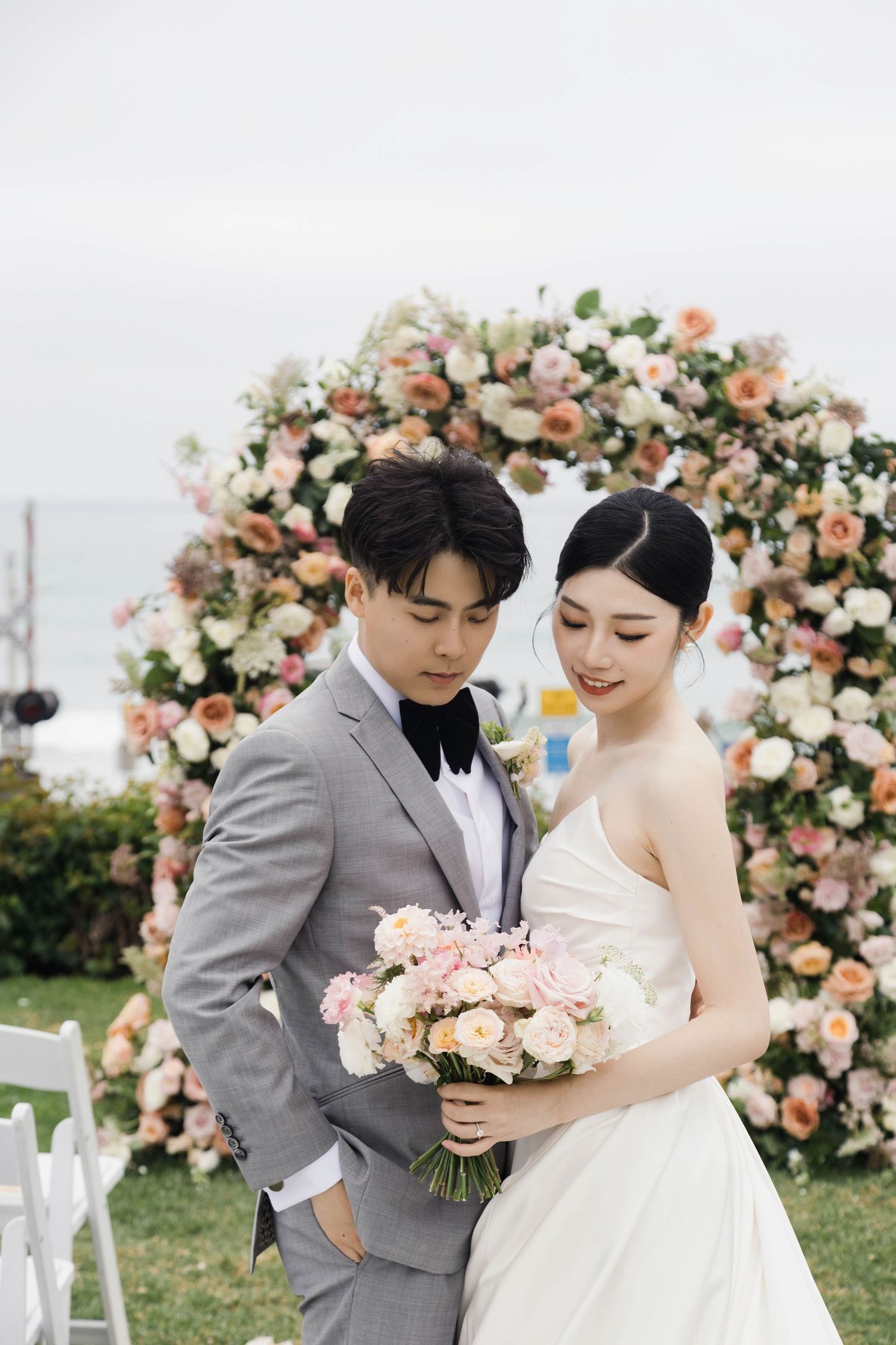 A romantic wedding photo shoot under a floral arch with pink and white roses in an outdoor garden setting.