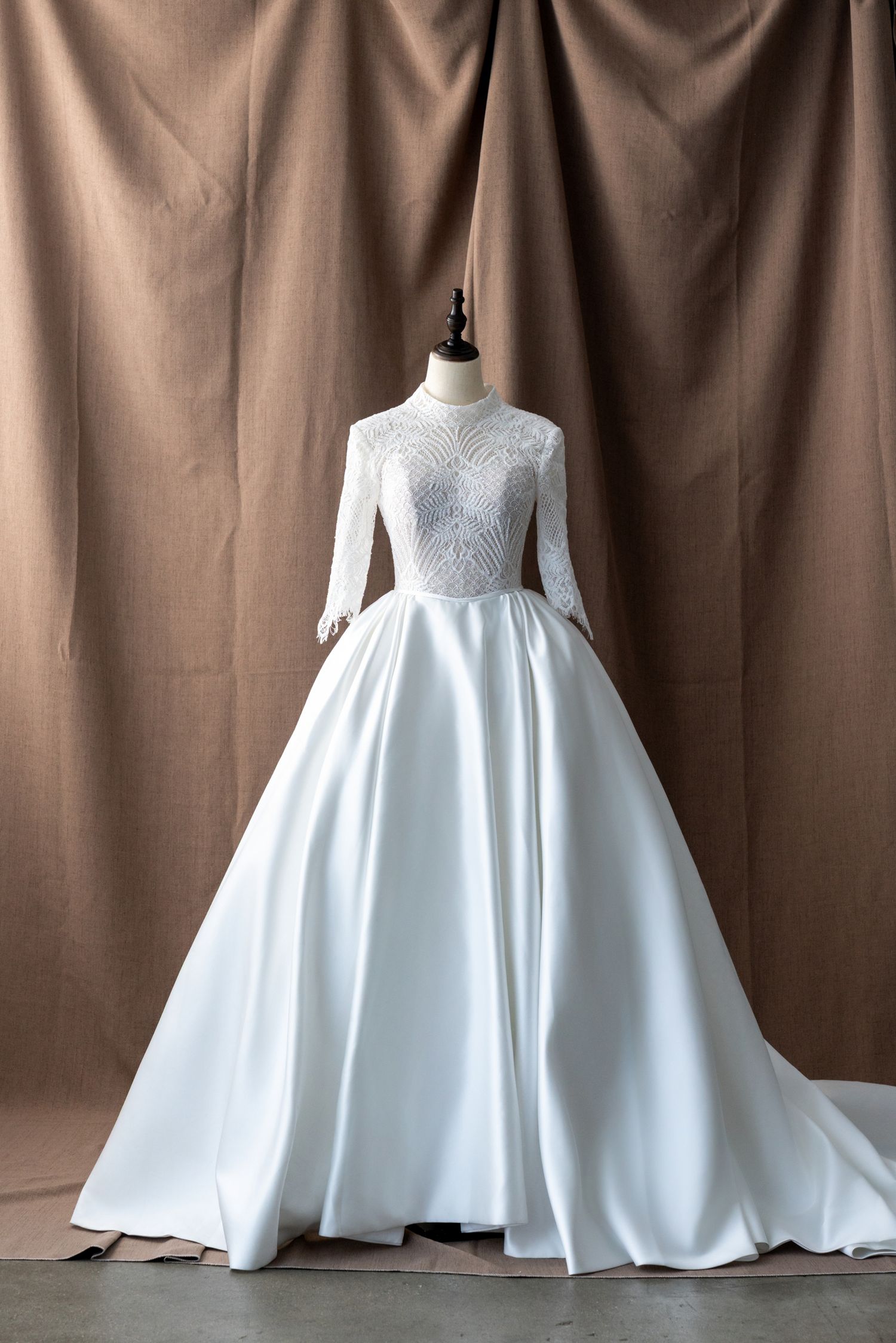 Full-length white satin wedding gown with lace bodice shown on dress form.
