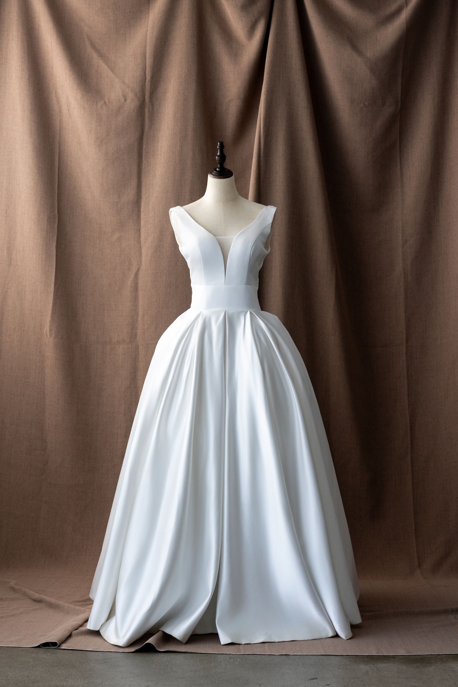 Minimalist white satin wedding ball gown with plunging back shown on dress form.