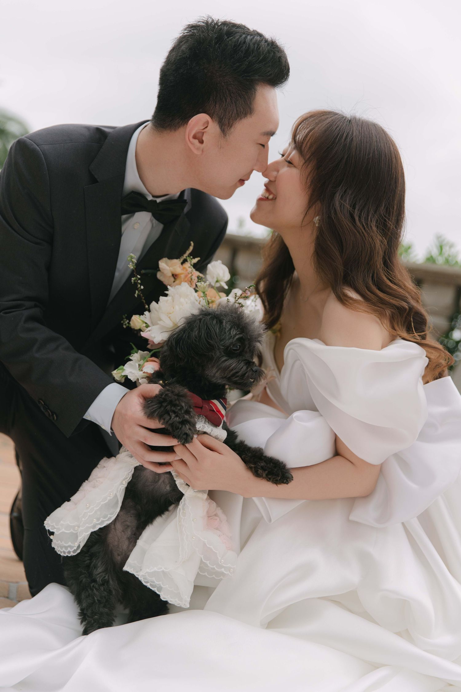Intimate wedding portraits with couple and their small black dog amid white dress and flowers.