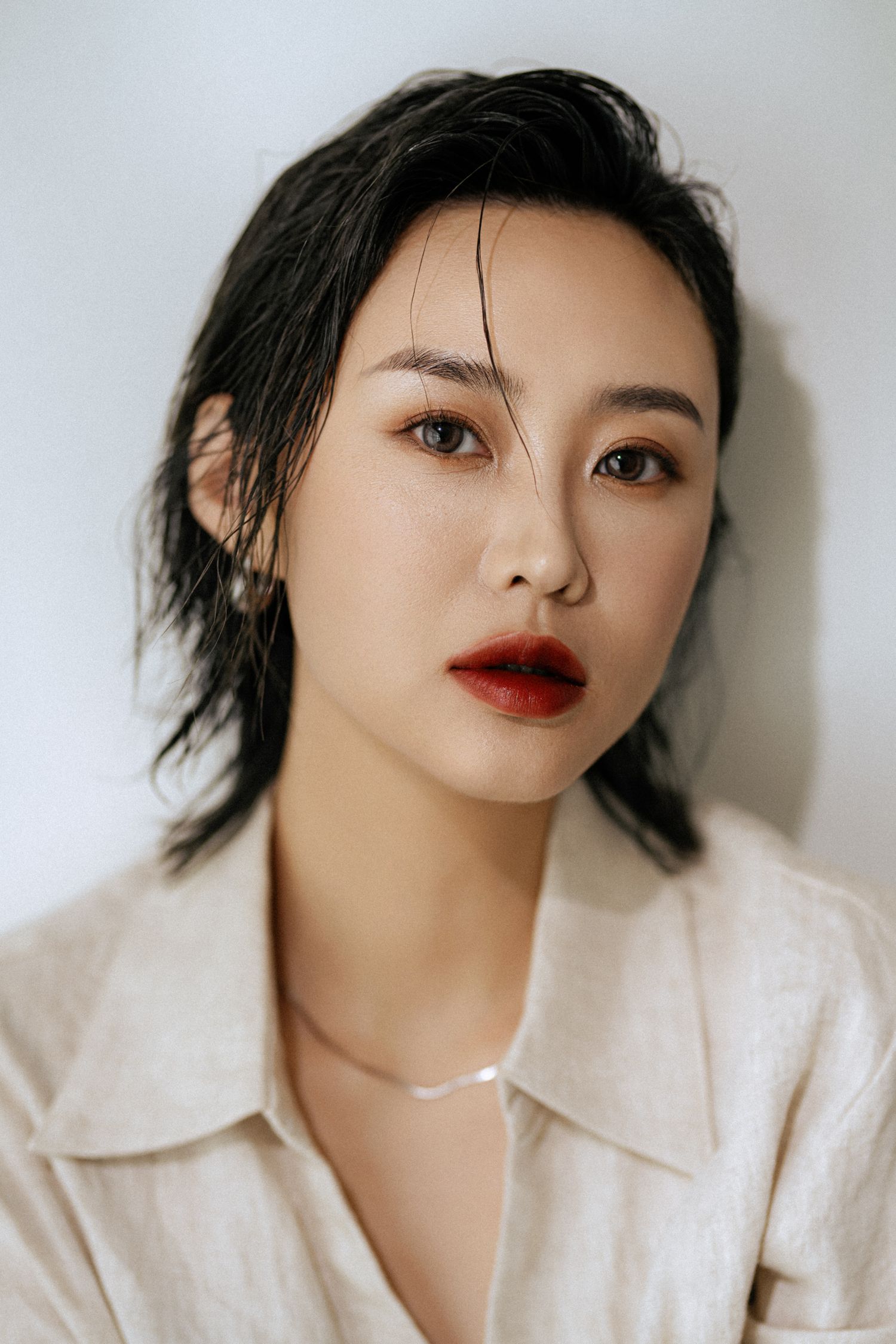 Dramatic close-up beauty shot with wet-look hair and bold red lipstick in white collar shirt.