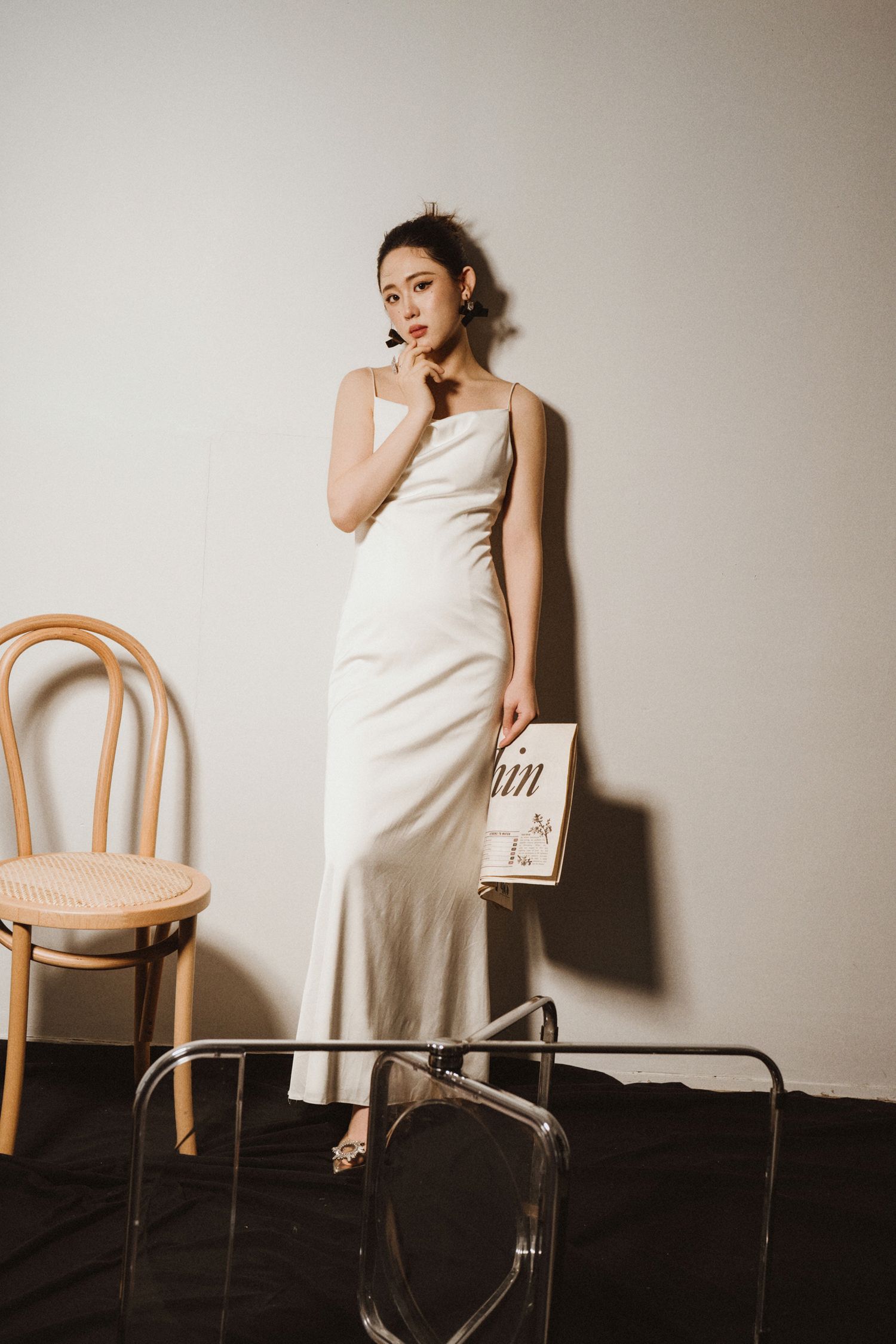 Dramatic studio portrait with wooden chairs and minimal styling against beige backdrop.
