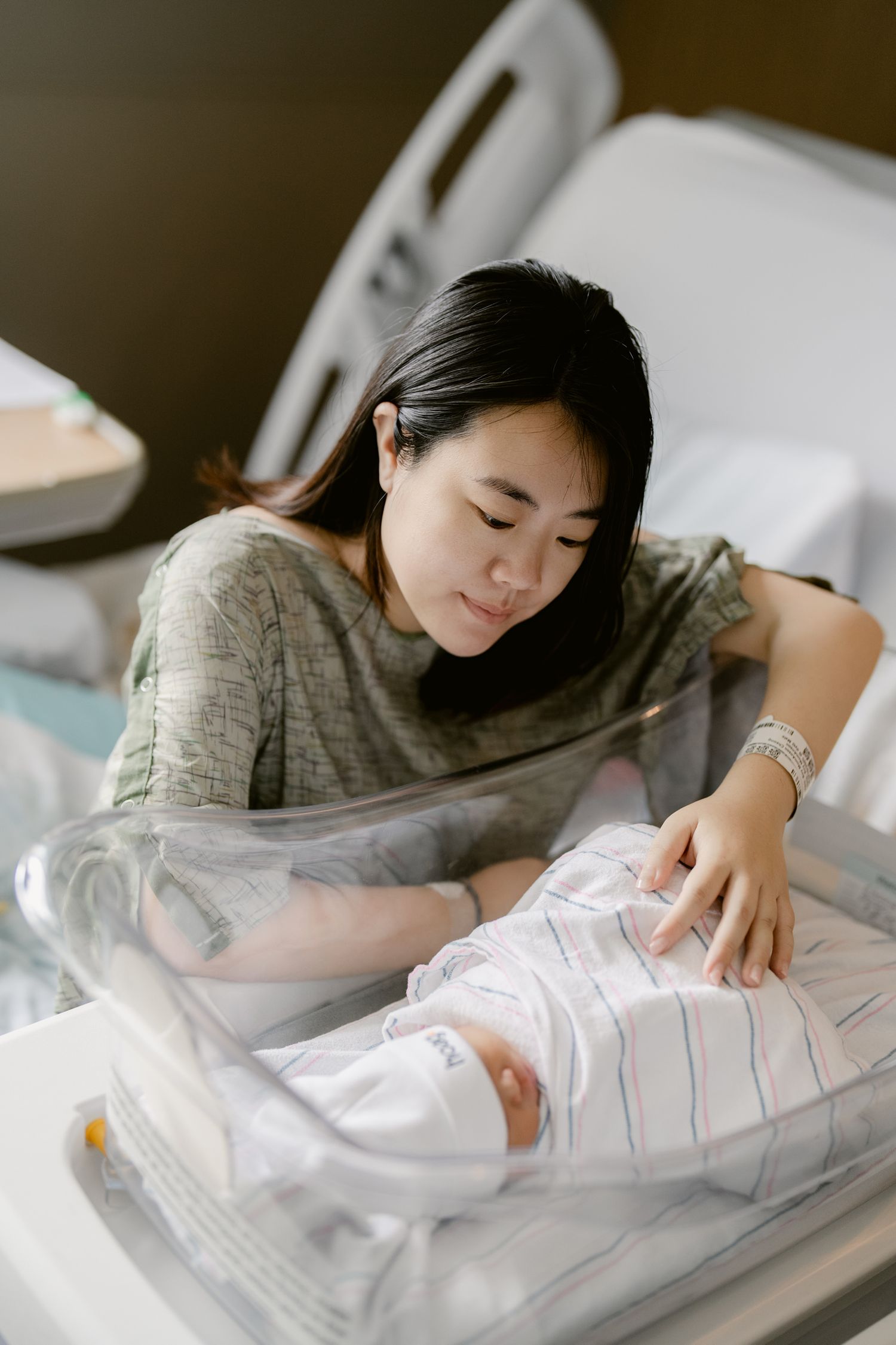 Person in grey shirt tenderly caring for infant wrapped in striped blanket.
