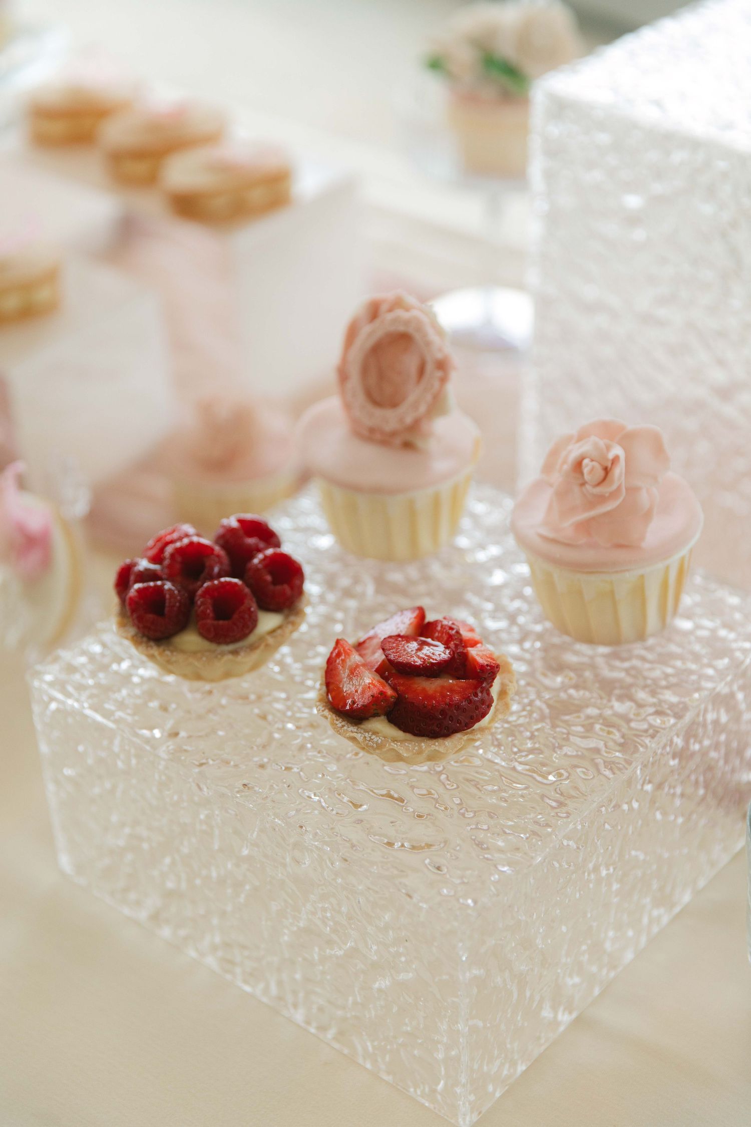 Delicate dessert display featuring pink macarons and fresh raspberries on a crystal platter.