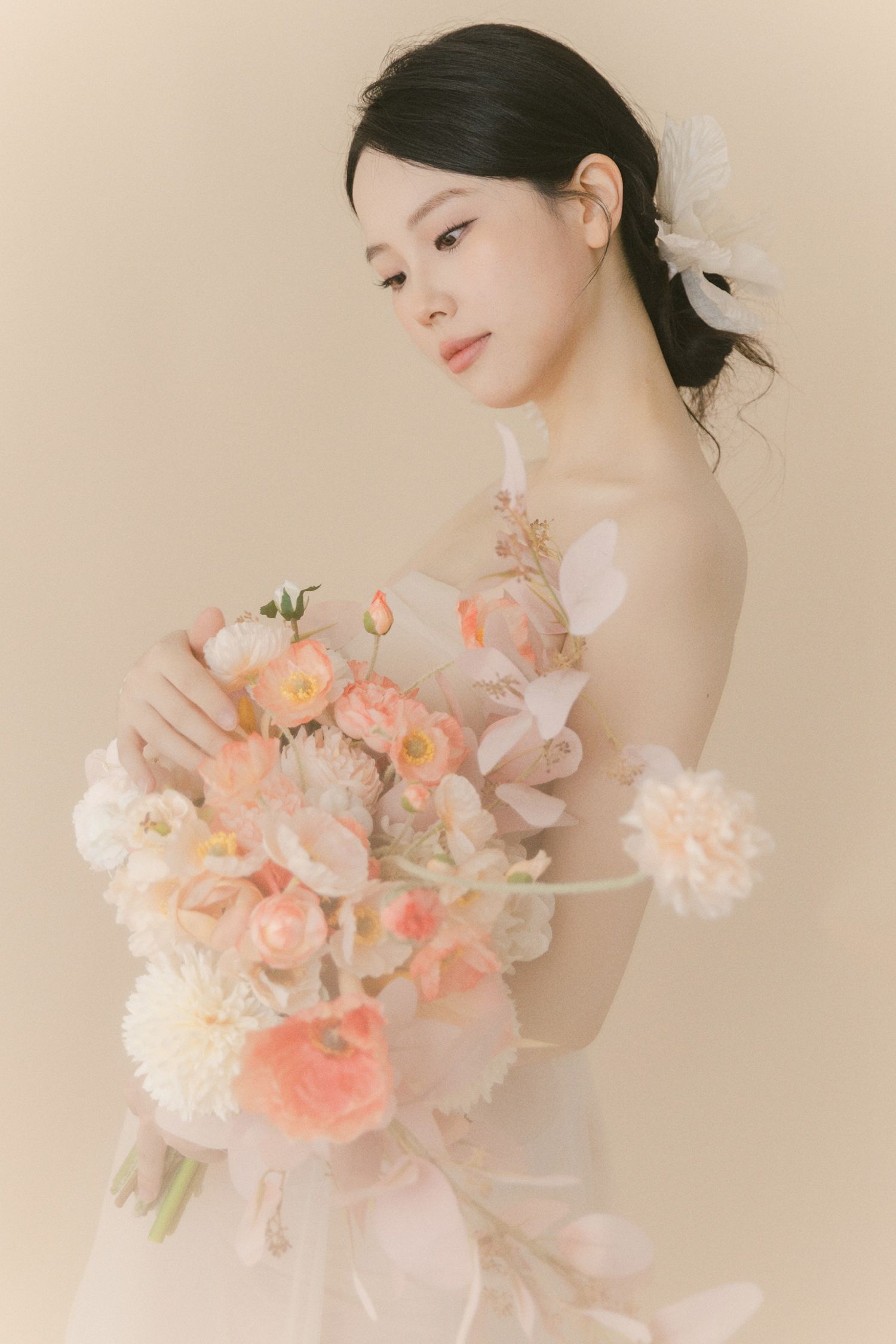 Artistic maternity portrait with coral and pink floral bouquet in soft natural lighting.