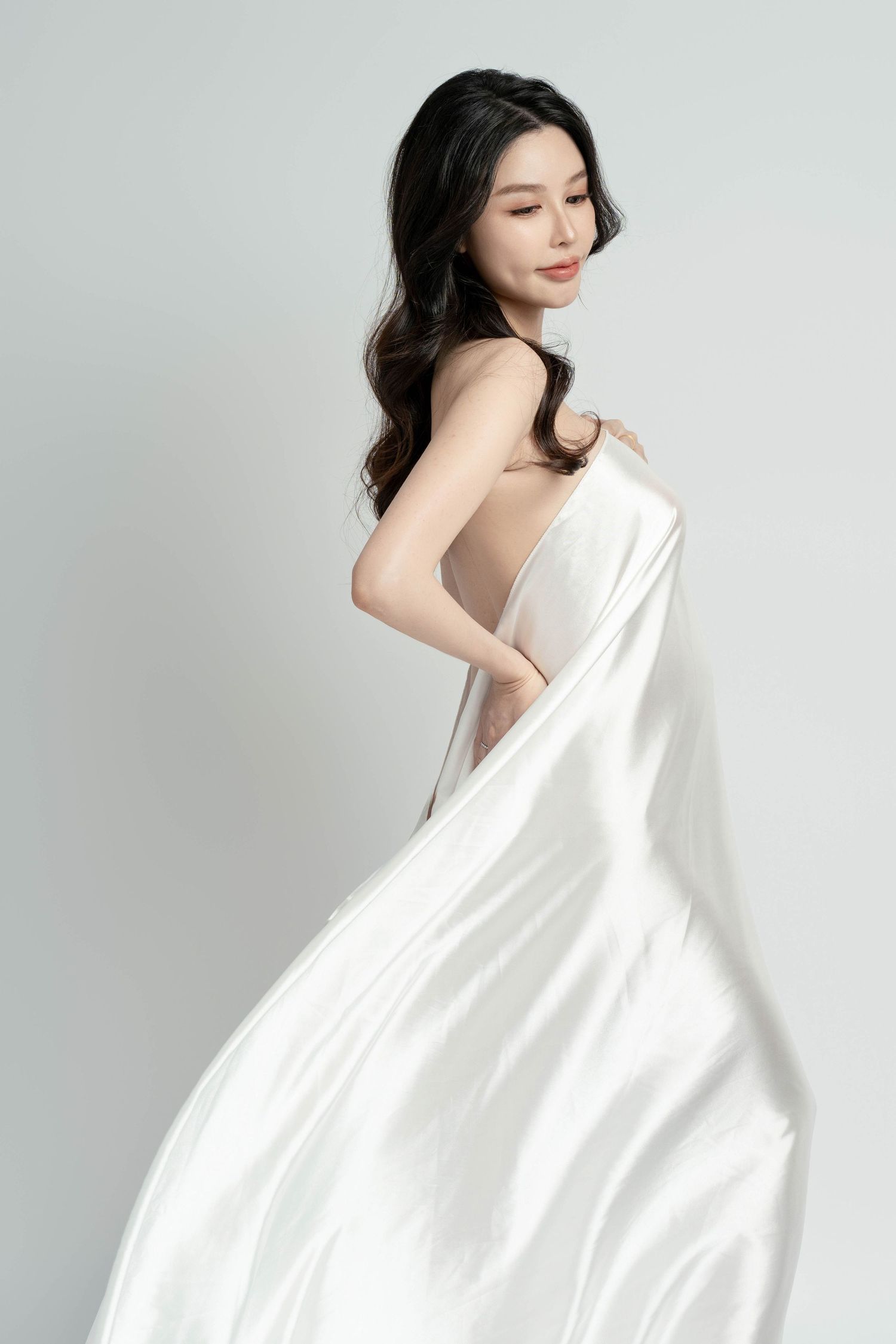 Elegant maternity portrait with white draped fabric in minimalist studio setting.