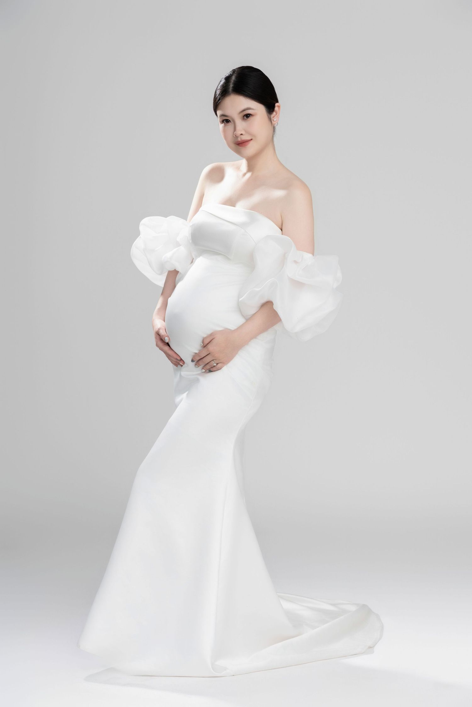 Dramatic maternity portraits in flowing white gown against light backdrop.