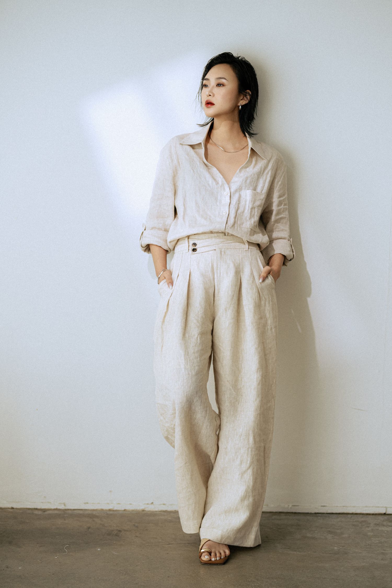 Model showcases oversized linen jumpsuit in neutral tones with relaxed silhouette.
