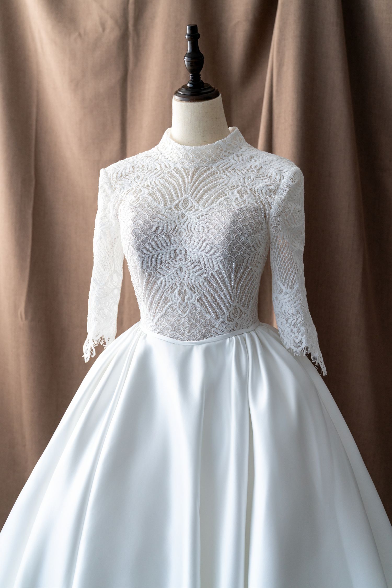 White lace bodice wedding dress with intricate beading and long sleeves displayed on mannequin.