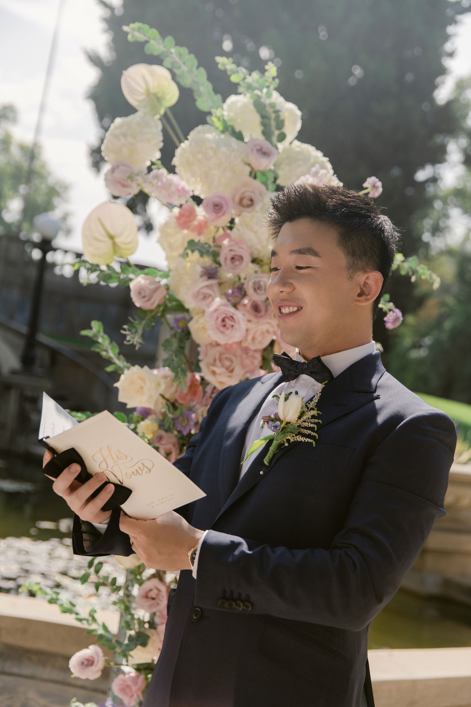 Person in navy suit reading from paper during outdoor wedding ceremony.