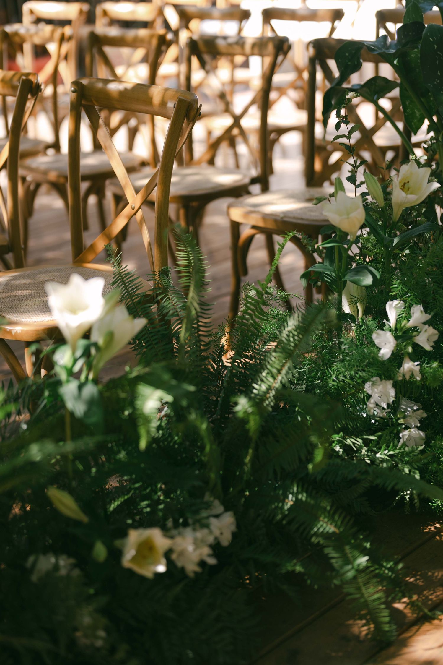 Cross-back wooden chairs and floral arrangements line an outdoor wedding ceremony space.