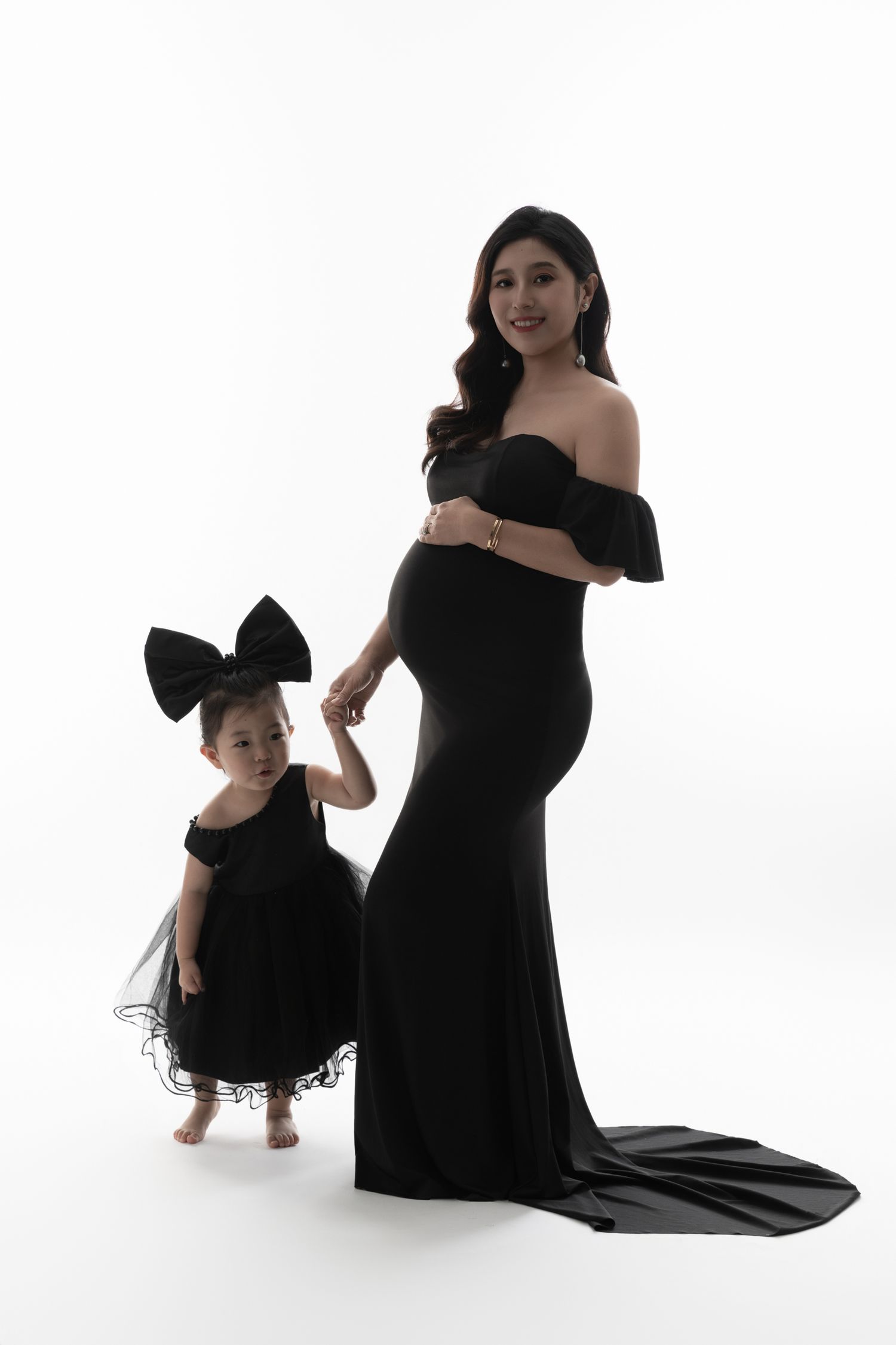 Mother and child in matching black formal dresses pose for studio portrait.