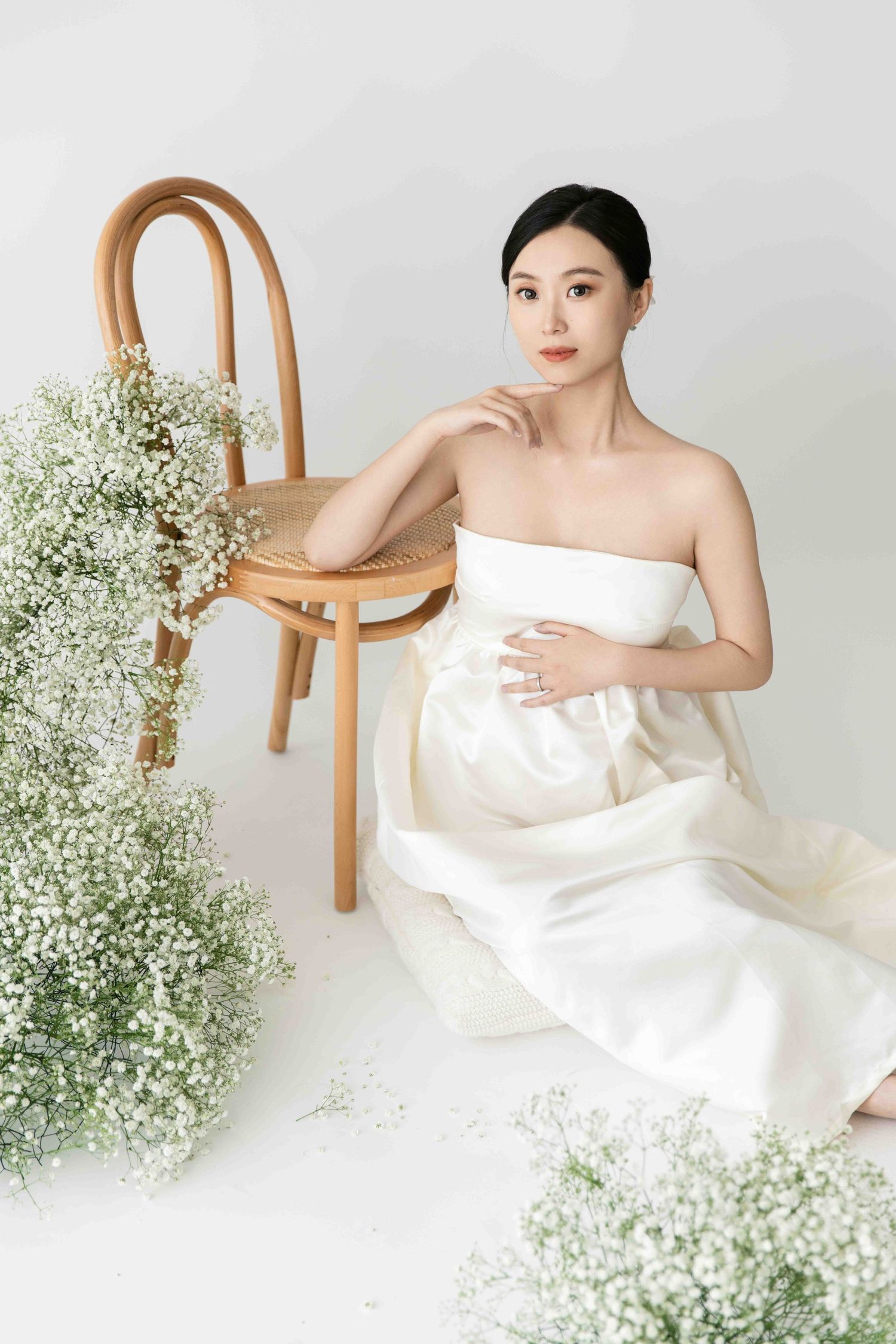 Clean minimalist maternity session with wooden chair and delicate baby's breath flowers.