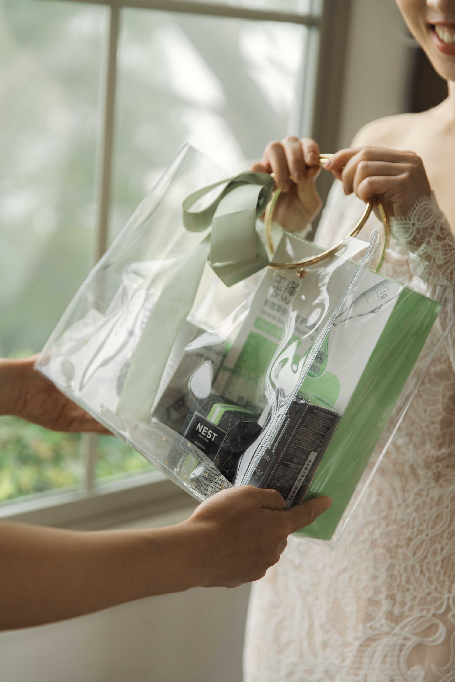 Hands holding clear plastic package against white lace wedding dress.