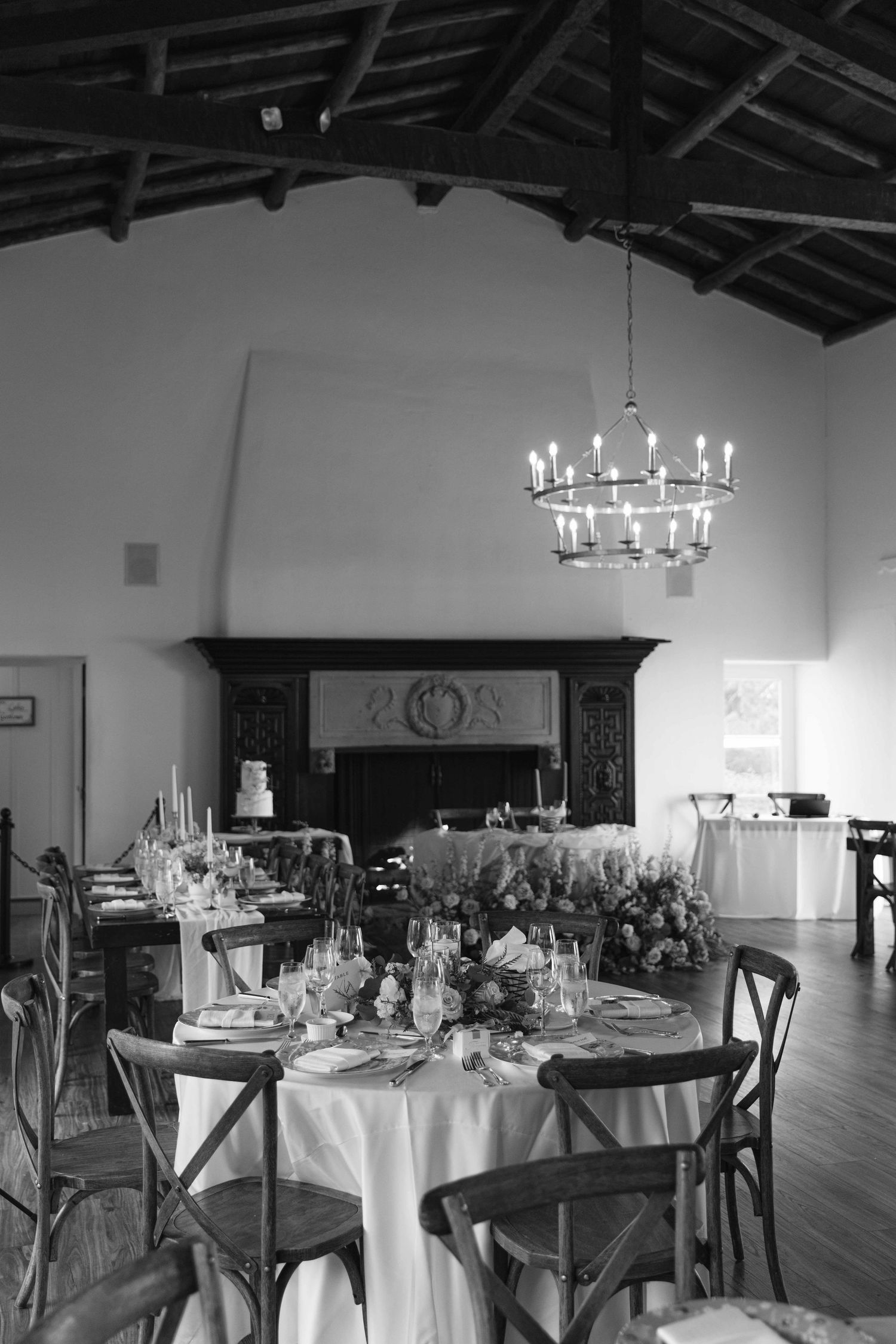 Black and white photo of an elegant reception hall with round tables and chandelier lighting.