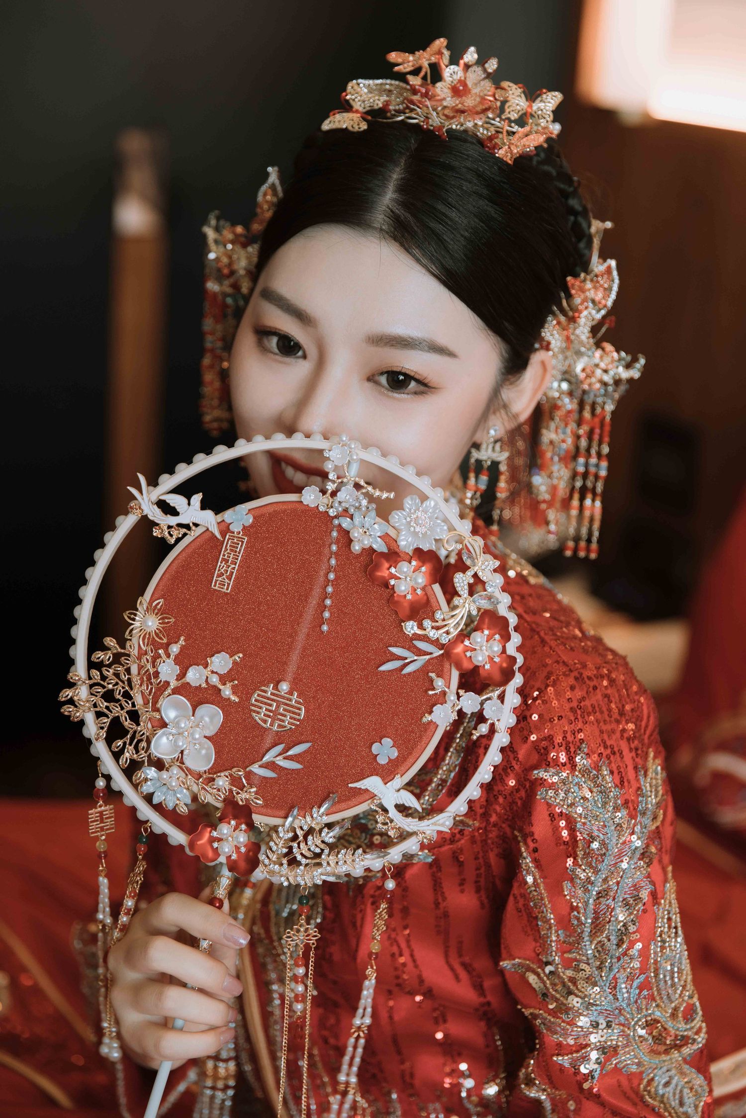 Person in red traditional Chinese dress holding decorative round fan with floral designs.
