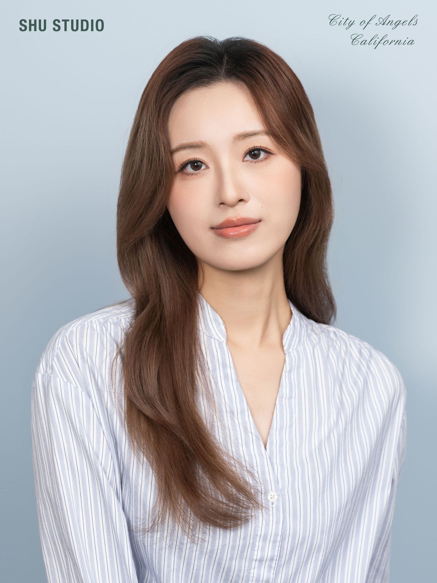 Professional headshot in white striped button-down shirt against light backdrop.