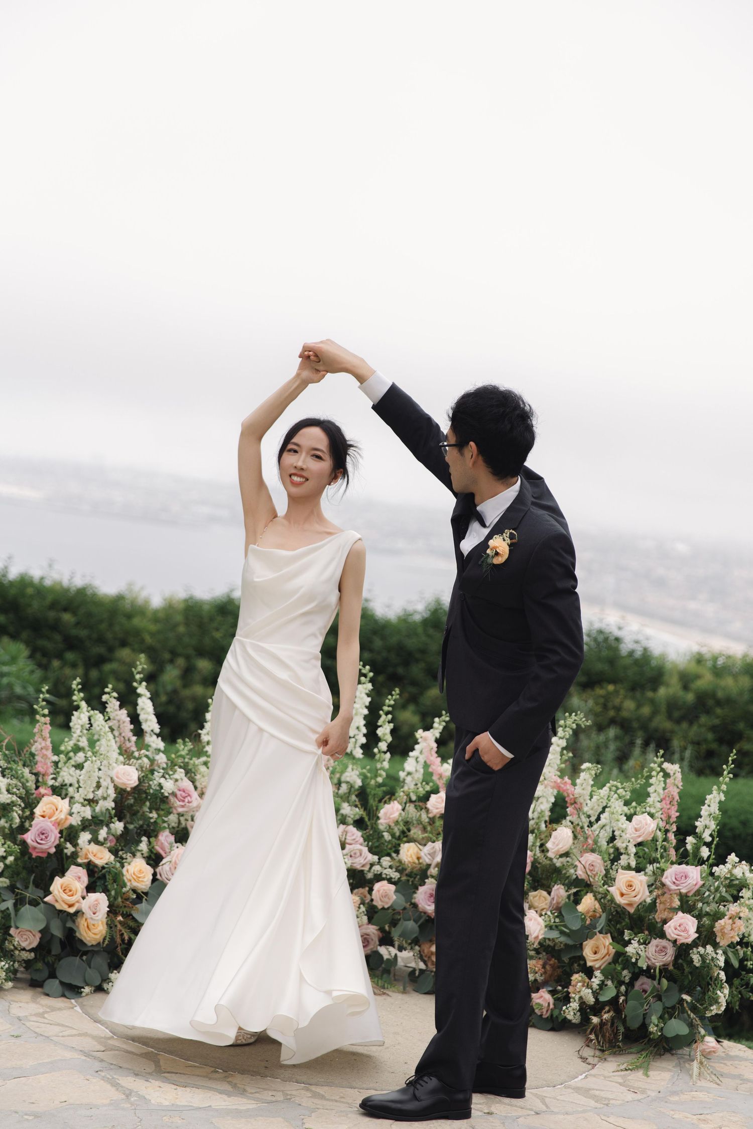 A couple dances together in a garden setting with beautiful roses and flowers in the background.