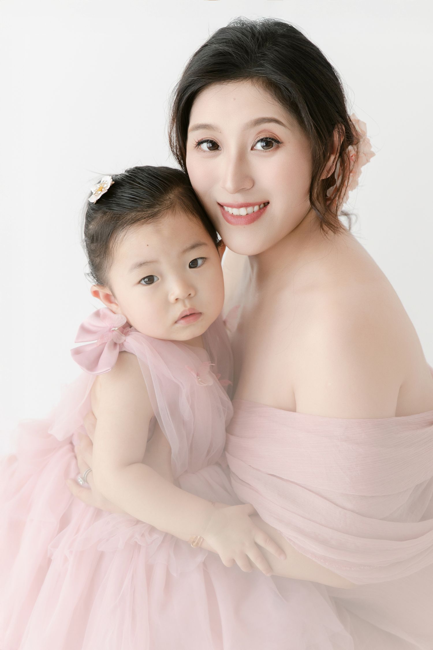 Mother and daughter in matching pink tulle dresses pose together against white background.