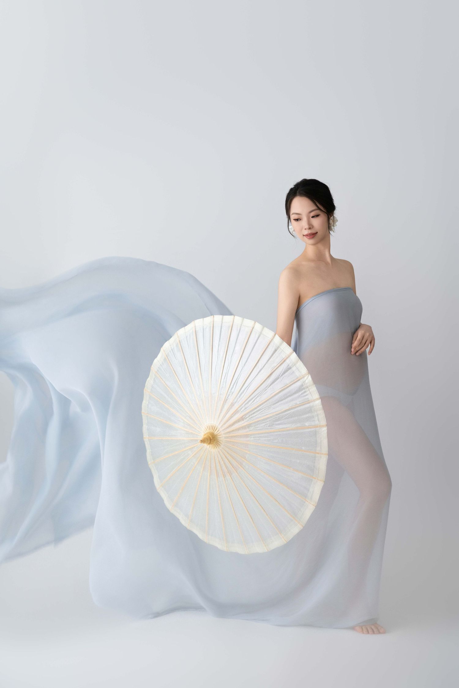 Minimalist maternity shoot with white paper parasol and light blue fabric.
