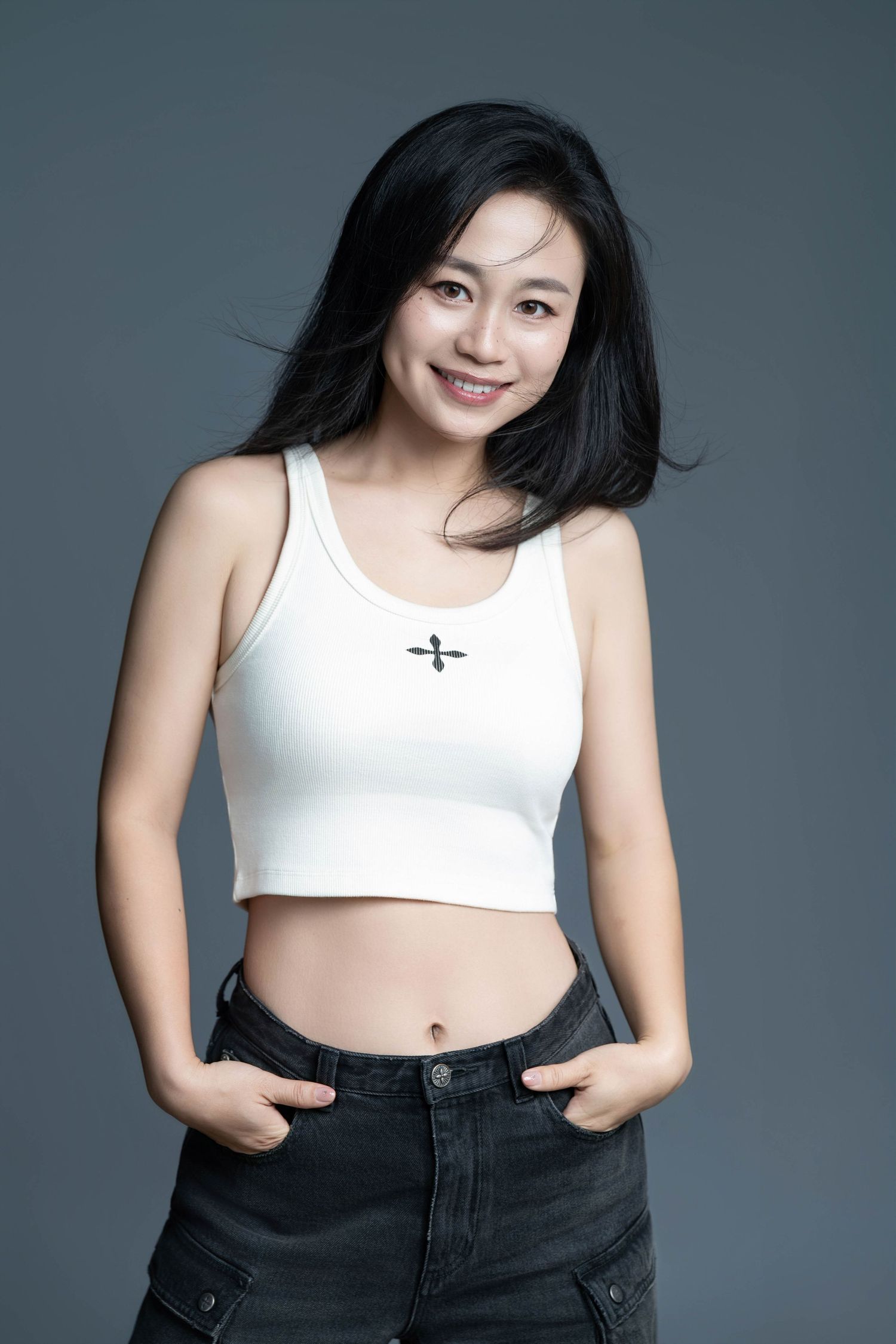 Casual fashion portrait in crop top and denim against studio background.
