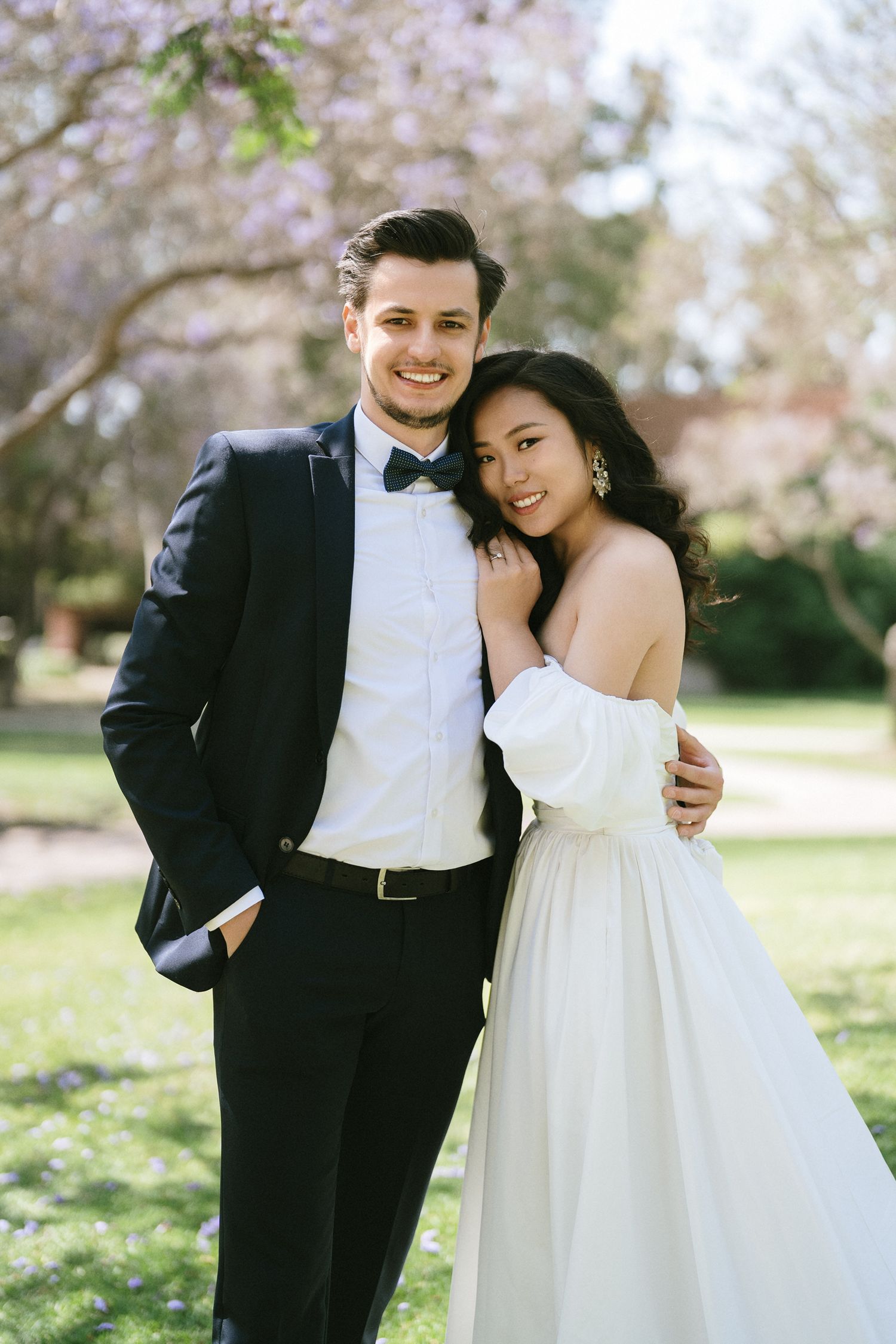 Wedding couple embracing under cherry blossoms in formal attire.