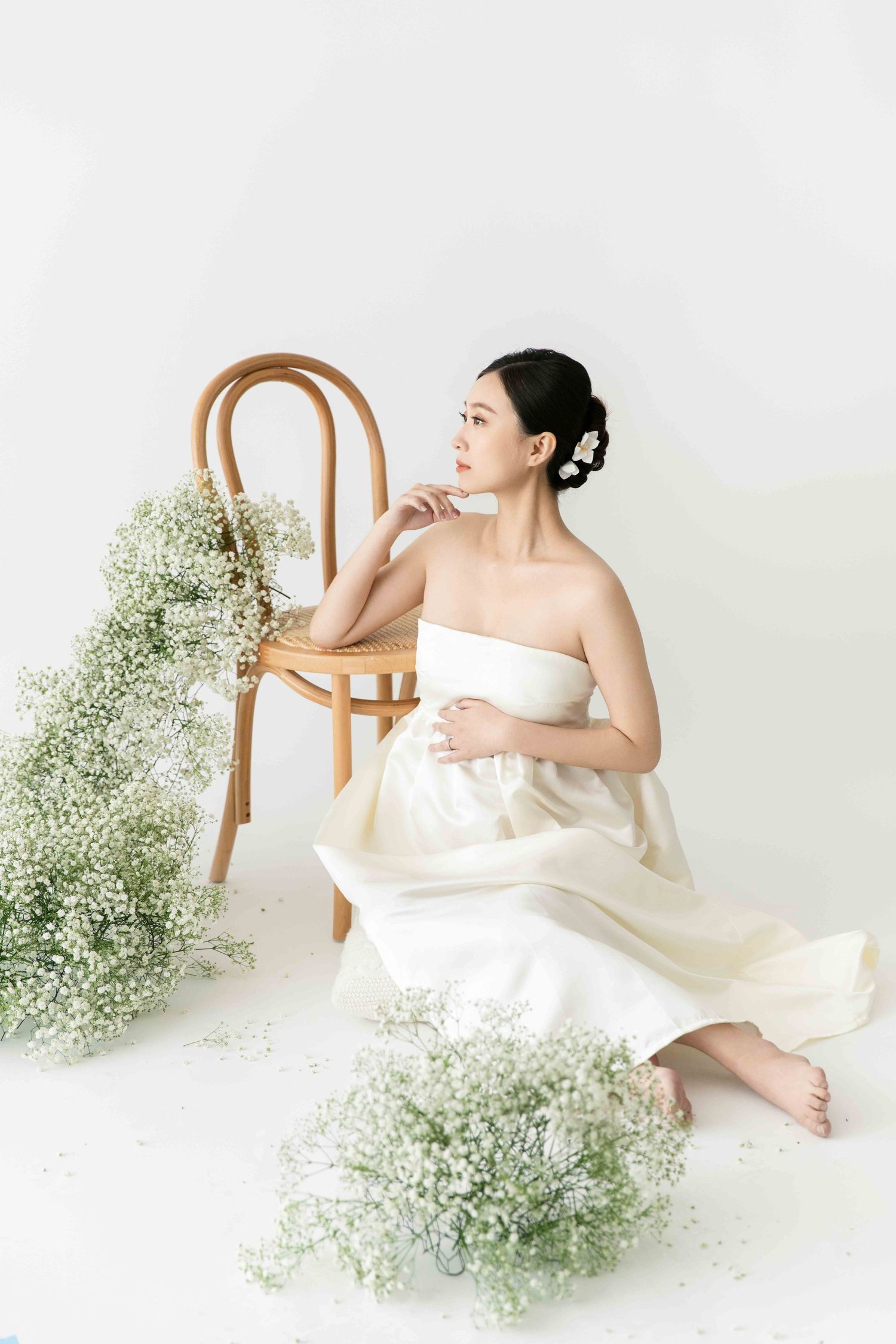 Serene maternity portrait with white dress and baby's breath flowers in bright studio setting.
